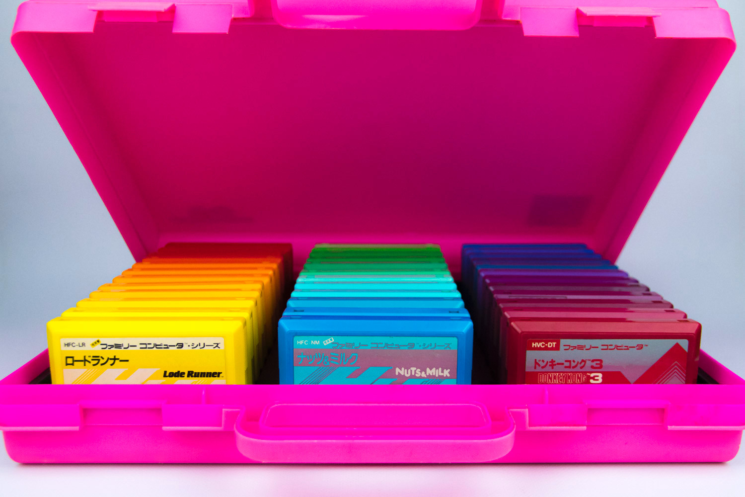 Multicolored Famicom cartridges arranged in a rainbow pattern inside a pink audio cassette storage case