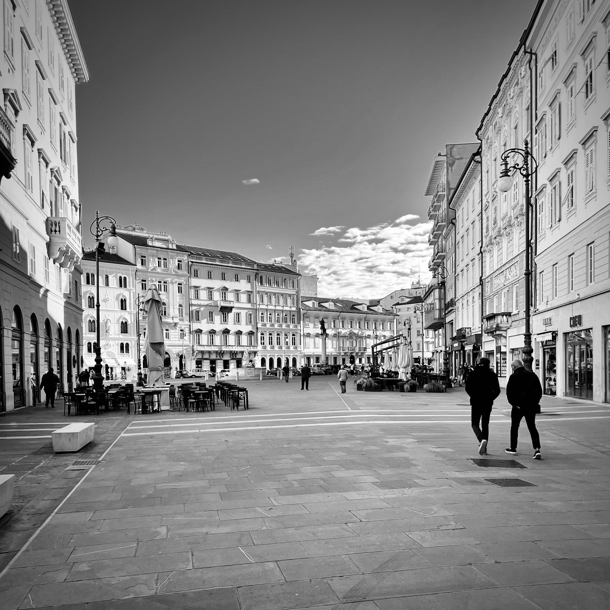 Sunday morning near deserted town square in Trieste with the odd figure and cafe tables not yet full.