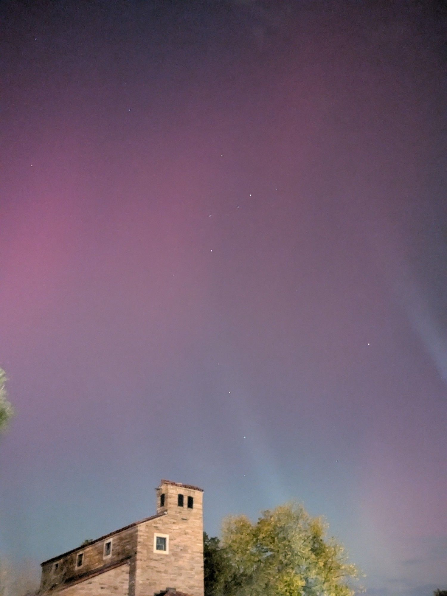 pinky red aurora with a hint of green over a building and tree