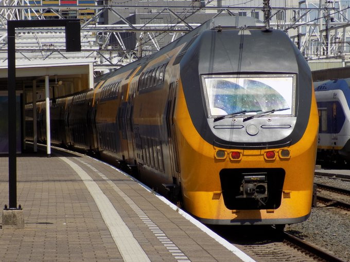 A zoomed-in photo of a Bombardier VIRM train in a bright yellow NS Intercity livery, loading passengers at Leiden Centraal before taking an eastbound journey to Amsterdam Centraal from Den Haag Centraal. 