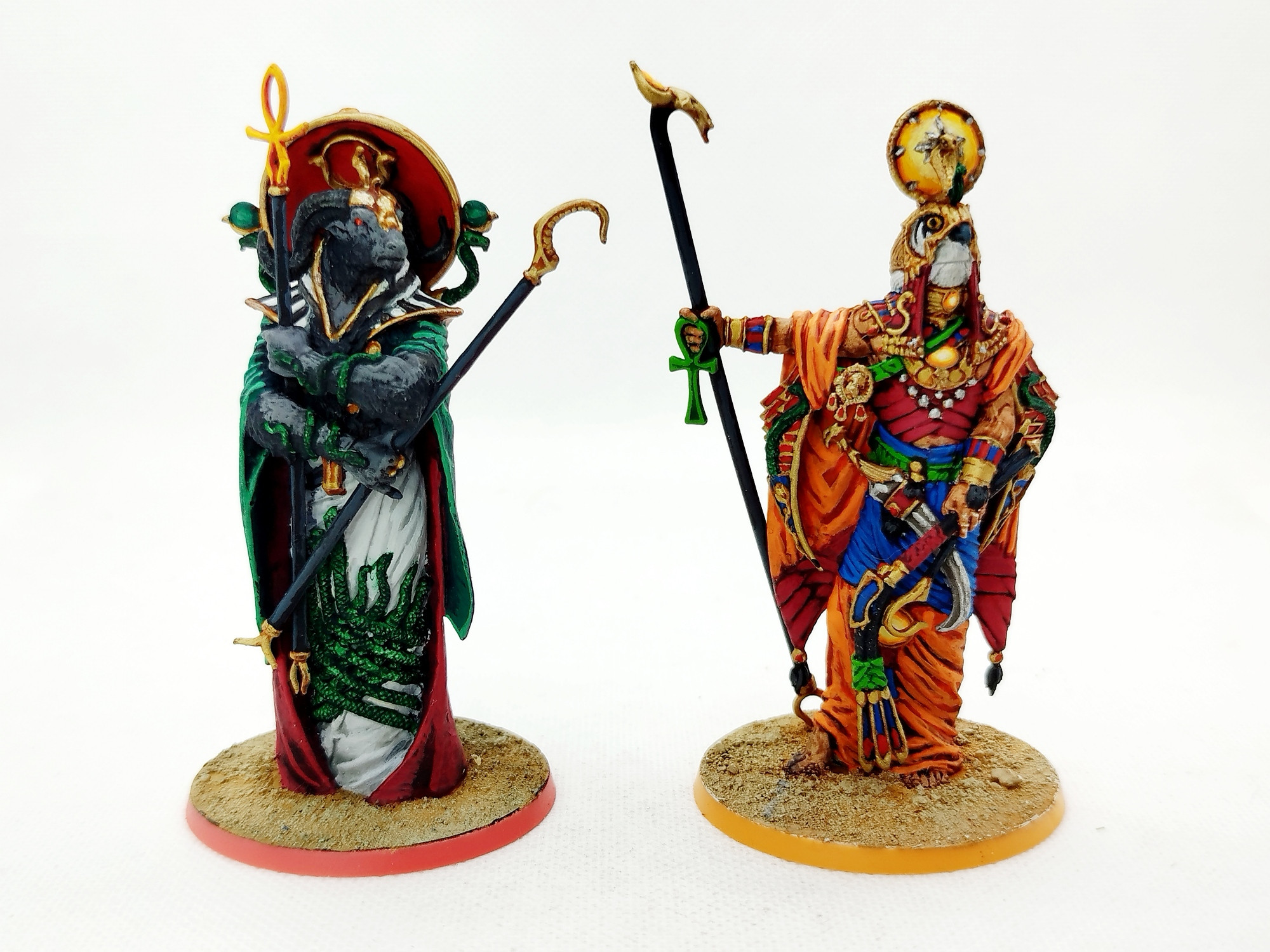 Foto de dos miniaturas de deidades egipcias sobre un fondo blanco, estando Amón a la derecha y Ra a la izquierda.

Amón tiene la apariencia de un carnero negro antropomórfico. Vestido con túnicas de colores verdes, rojos y blancos, varias serpientes están enredadas en sus brazos y vestimentas. Sobre su espalda porta un gran disco de color rojo. En ambos brazos lleva distintos cetros, acabado en una ornamentación con forma de hoz y el otro acabado en un Ankh que brilla incandescente.

Ra se ve como una persona con cabeza de halcón. Como dios del sol porta túnicas de colores cálidos, principalmente de color naranja y rojo. Aunque también tiene algunas de colores azules y verdes. Tiene un disco coronando su cabeza el cual, al igual que varias gemas que adornan su vestimenta, emiten luz como pequeños soles. En su brazo derecho porta un cetro y en el izquierdo un látigo.