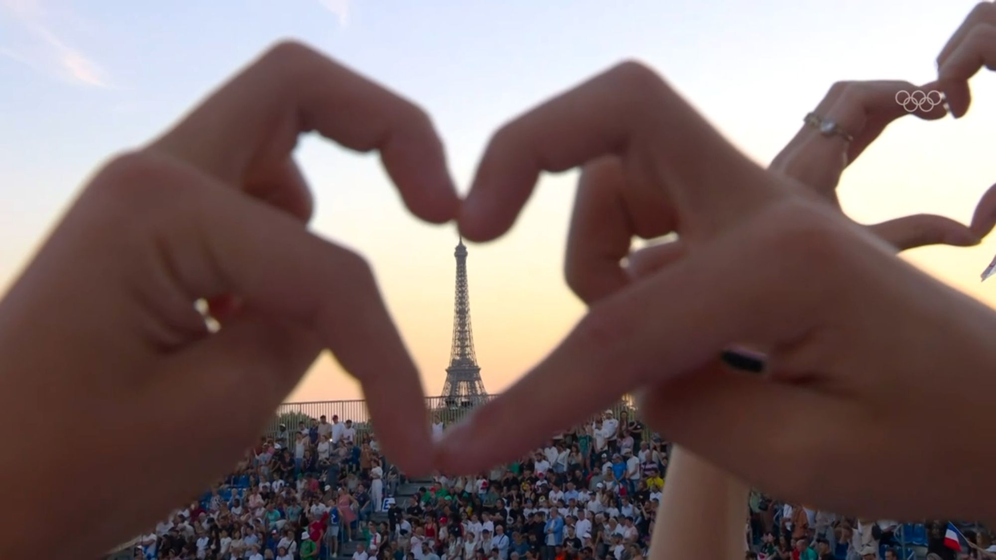 the eiffel tower at sunset, someone in the crowd is making a heart sign around it