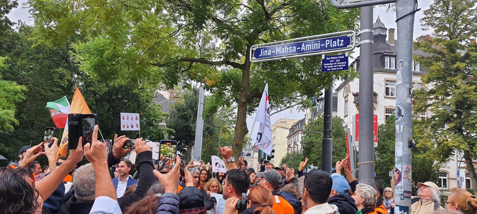 Bild der Kundgebung, darüber ist das Straßenschild zu sehen