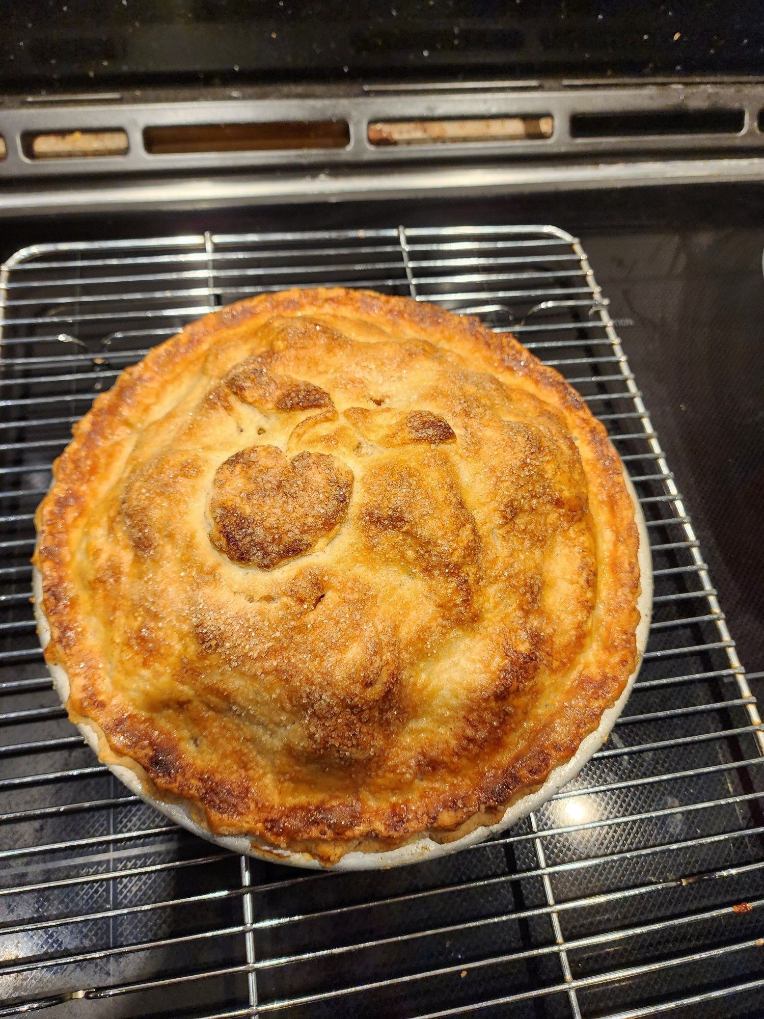 Apple pie on a black stovetop. There's an apple and leaves marked out in dough on the top.