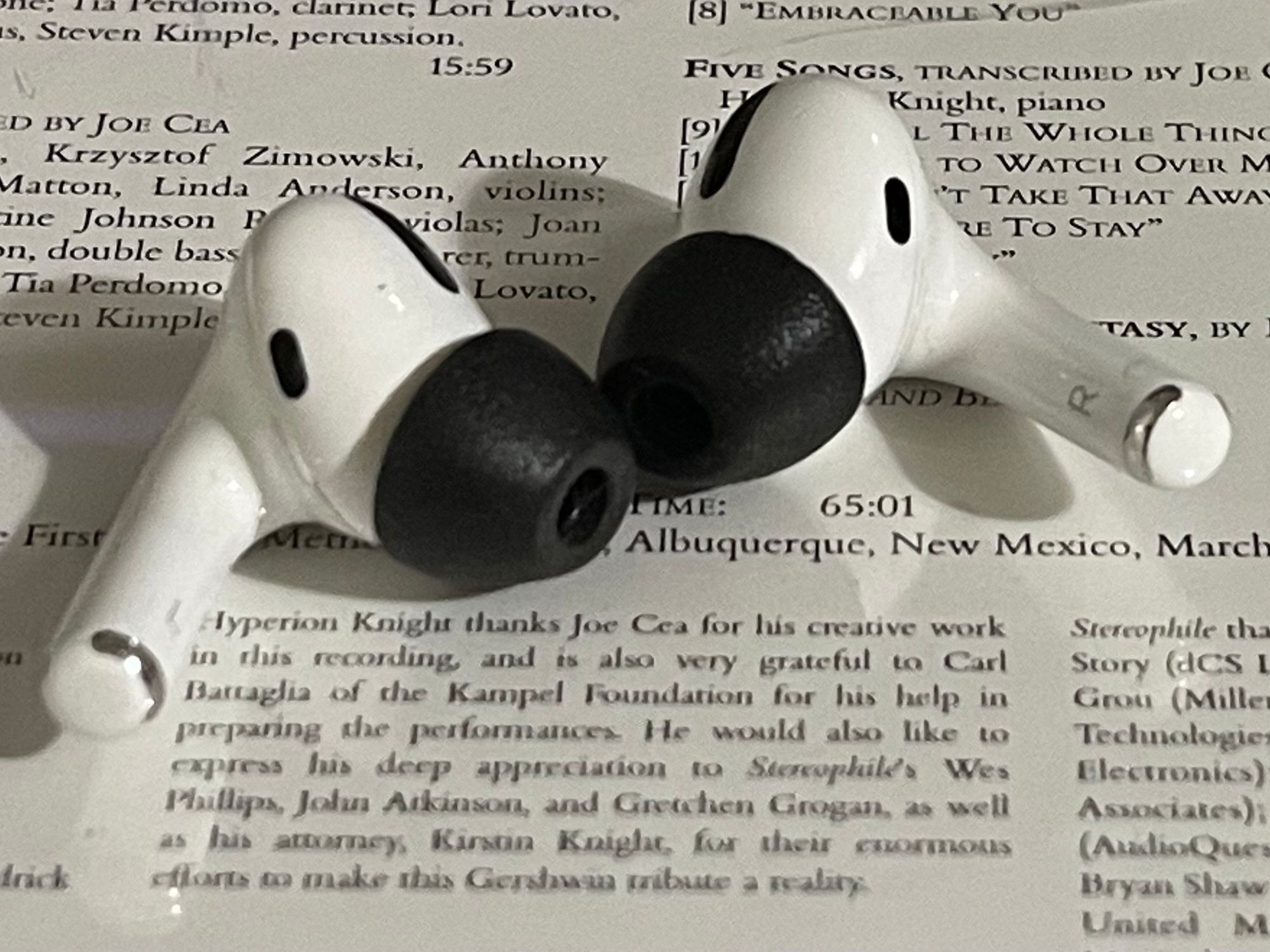 A close up photograph of a pair of Apple AirPods Pro with freshly replaced Comply foam tips sitting on the back of a classic music CD case (Rhapsody: Works for Piano & Orchestra by George Gershwin, Hyperion Knight , Pianist and Conductor, Sterophile 1997).