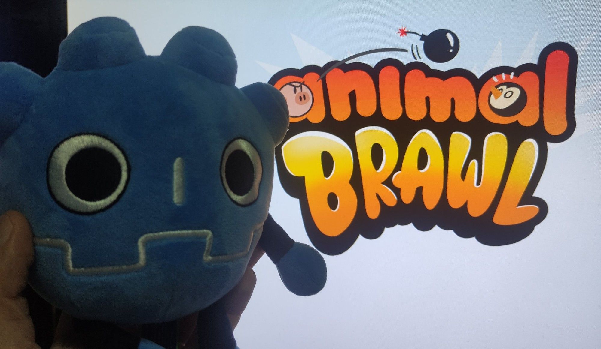 El peluche de Godot delante de la pantalla en la que está el logo de Animal Brawl