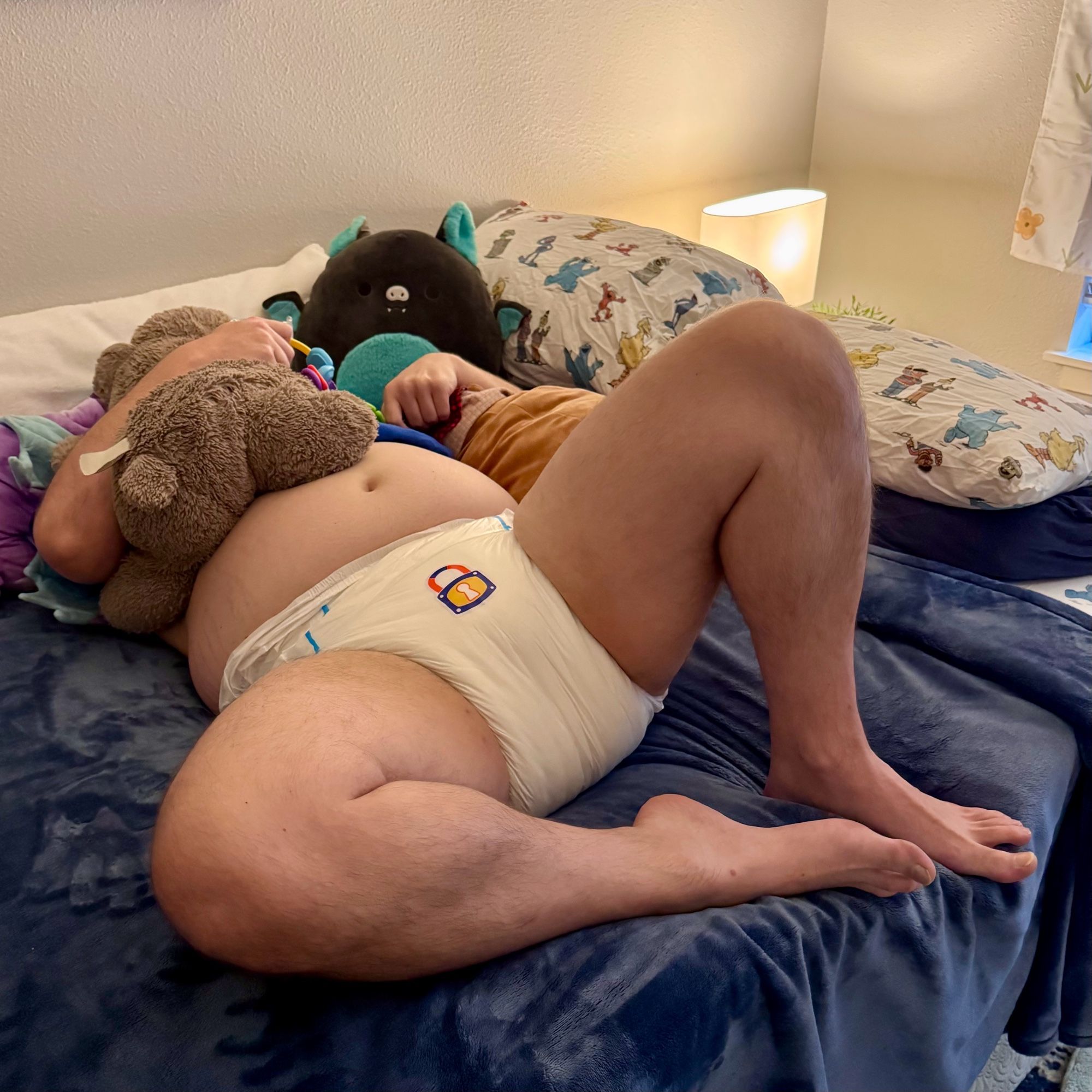 Boy in a diaper with a lock sticker trying to hide behind his plushies