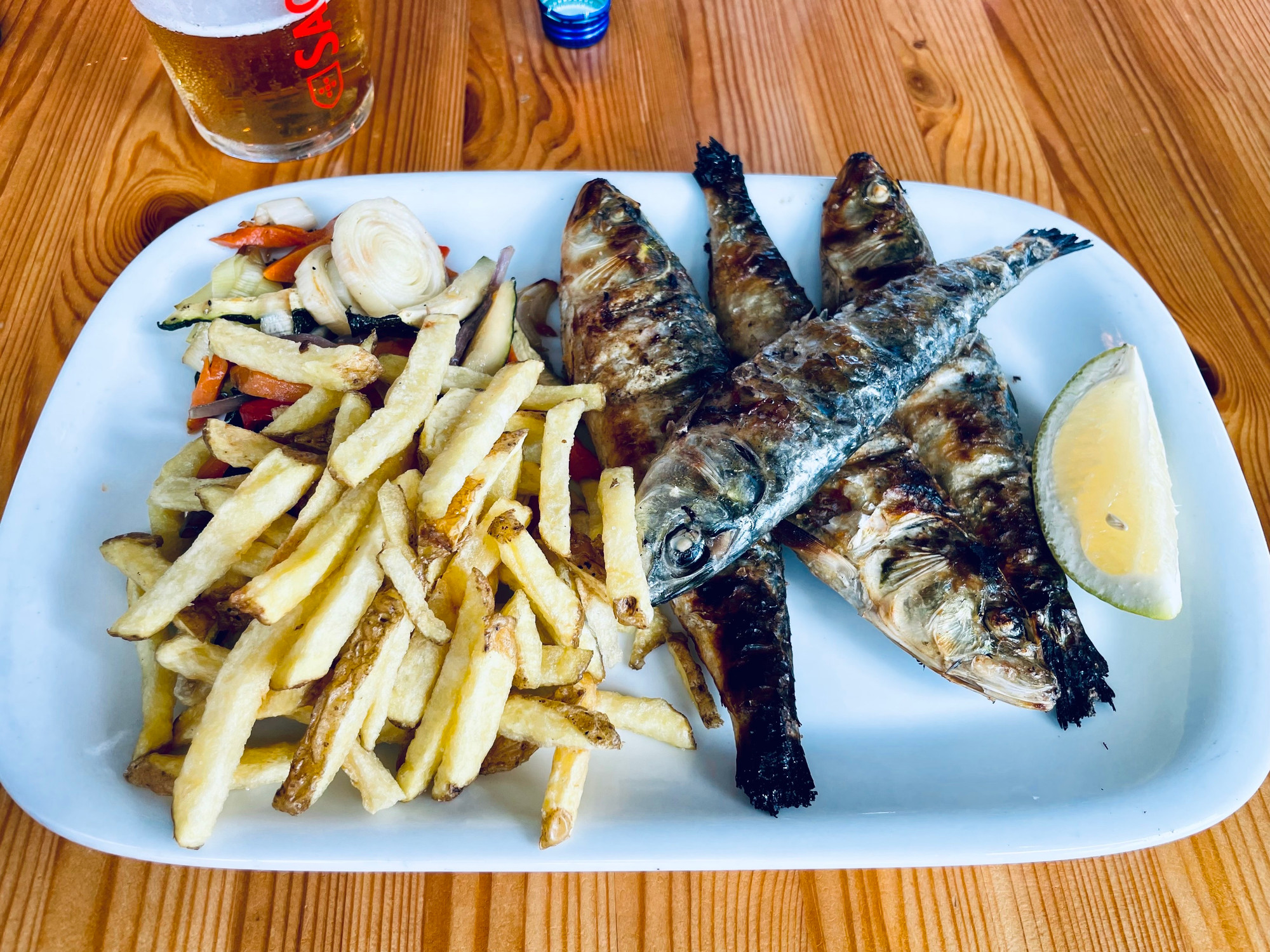 A plate with four grilled sardines and fries. 