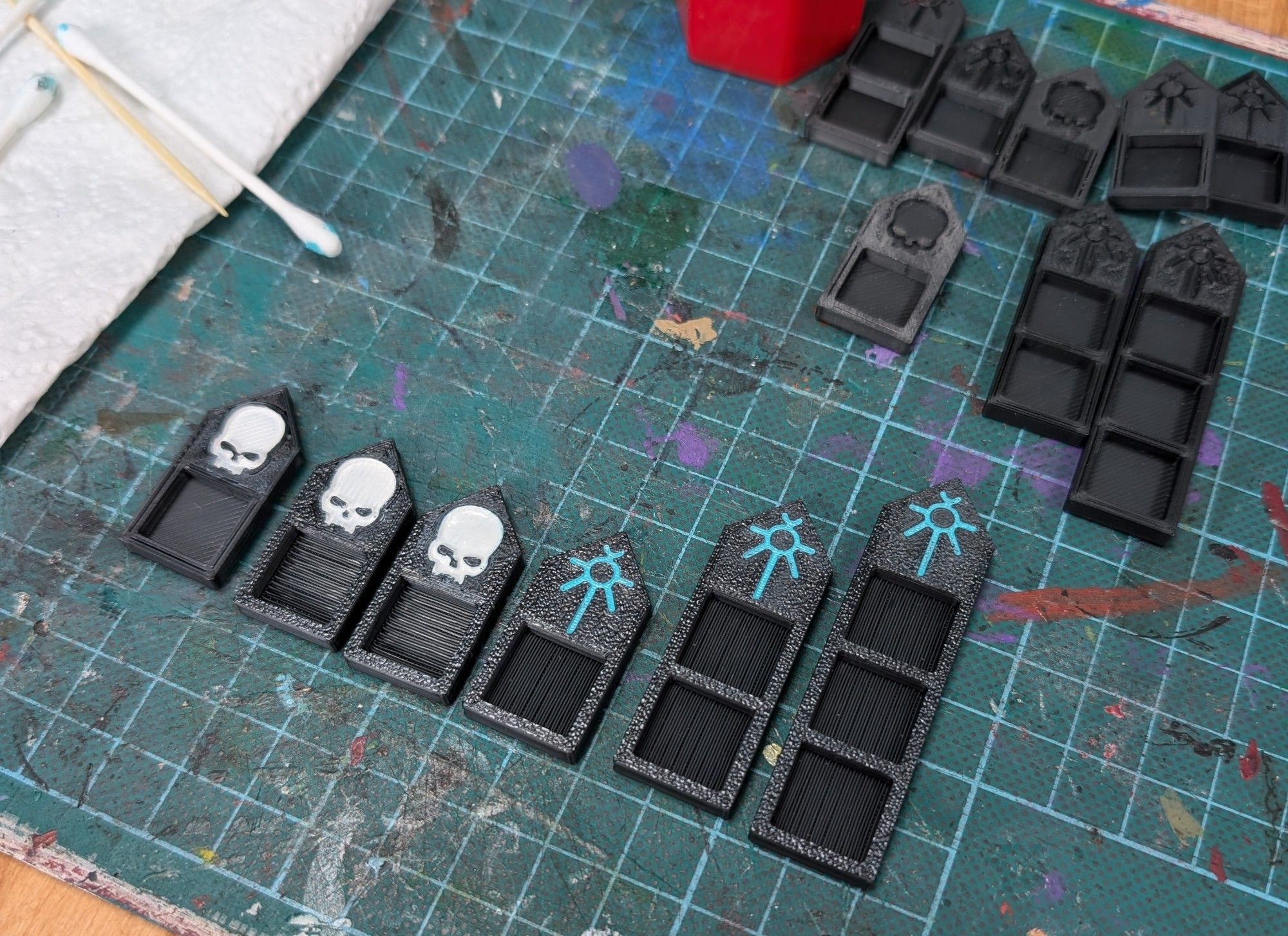 3D printed wound markers, to hold 12mm dice. Printed in black, 3 have a recessed skull motif in white, 3 have a green Necron glyph 