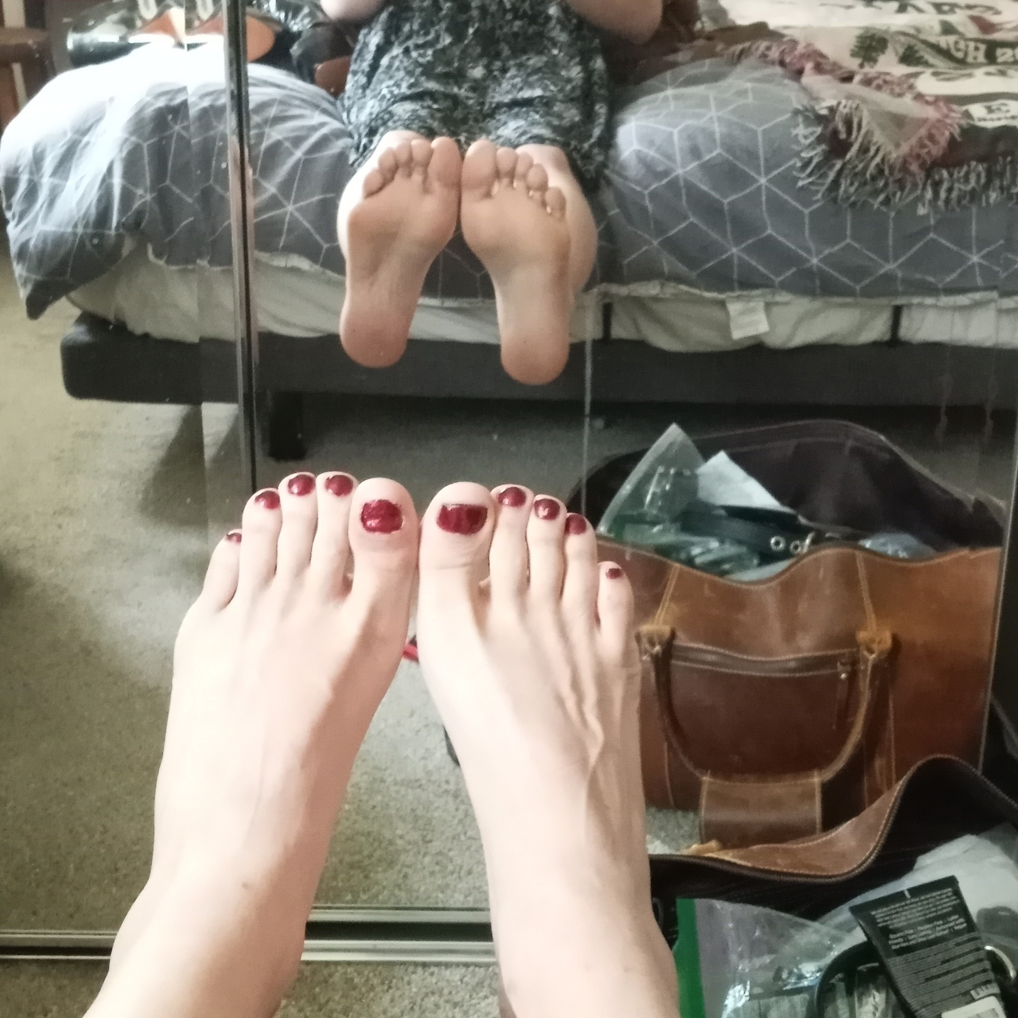 Meli in front of a mirror with her feet out. Red nail polish on the toes, tops of the feet showing at the bottom of the frame.

A reflection of Meli's soles hovers directly above