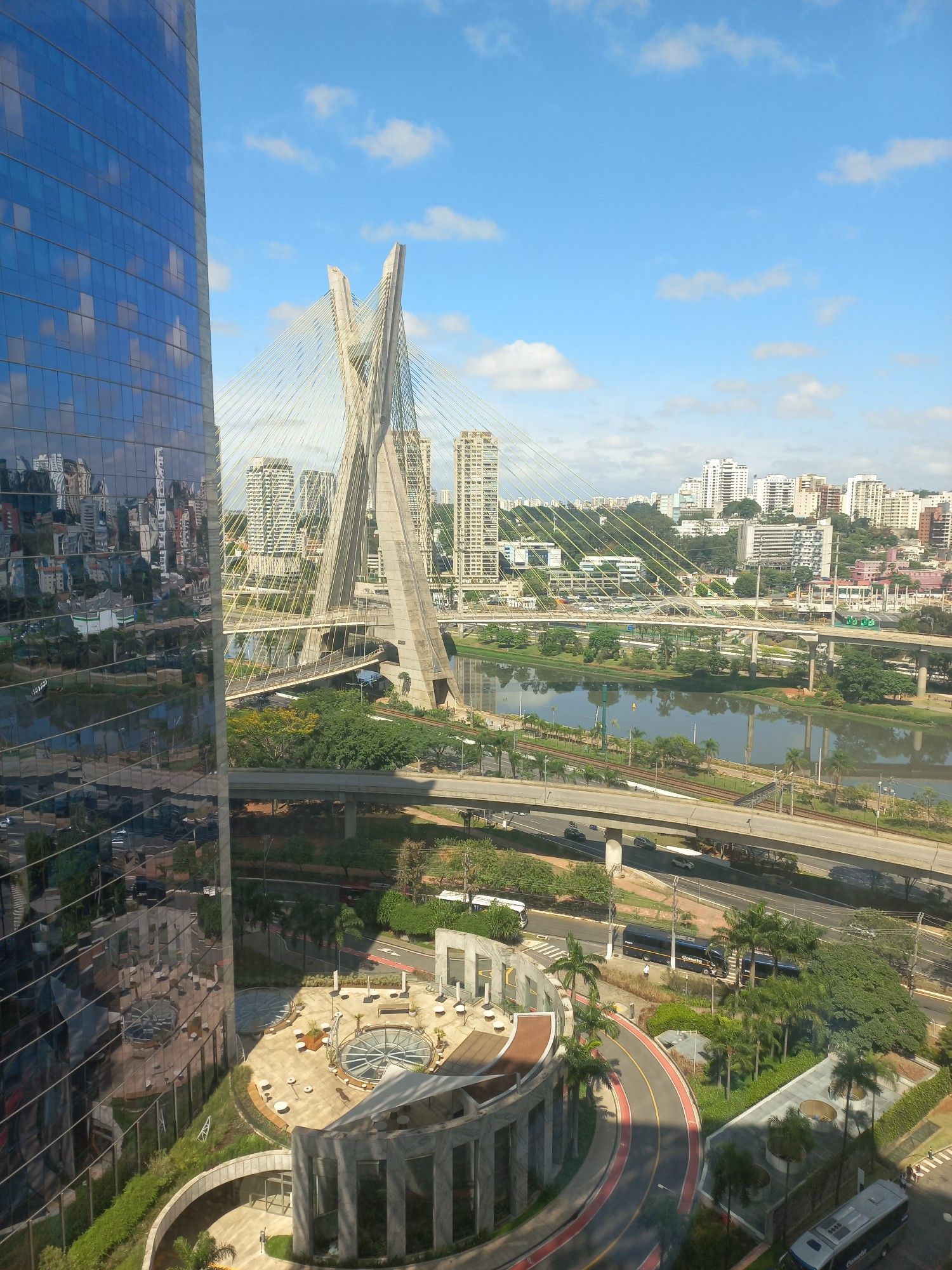 Vista próxima ao Rio Pinheiros, com prédio de escritórios, a Ponte Estaiada e a Marginal