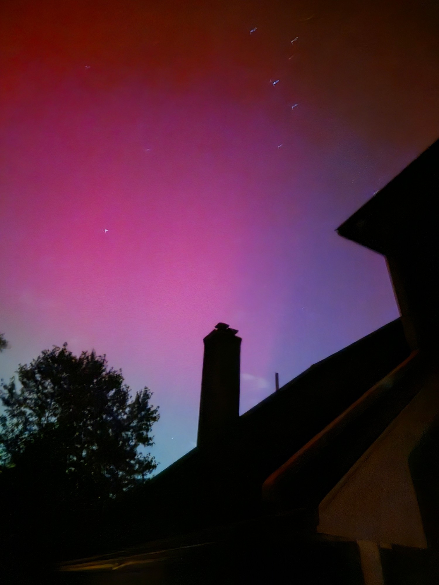 The Northern Lights in pink, purple, abd green above a chimney and tree