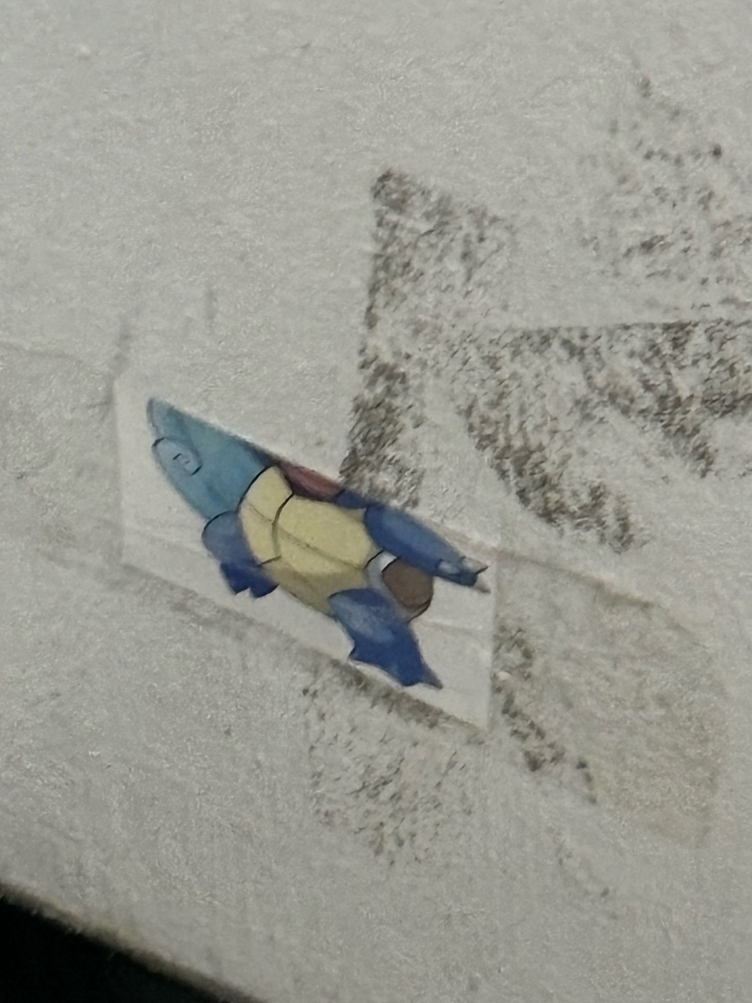 Half a sticker of squirtle stuck onto the wall with tape with tape marks on the wall