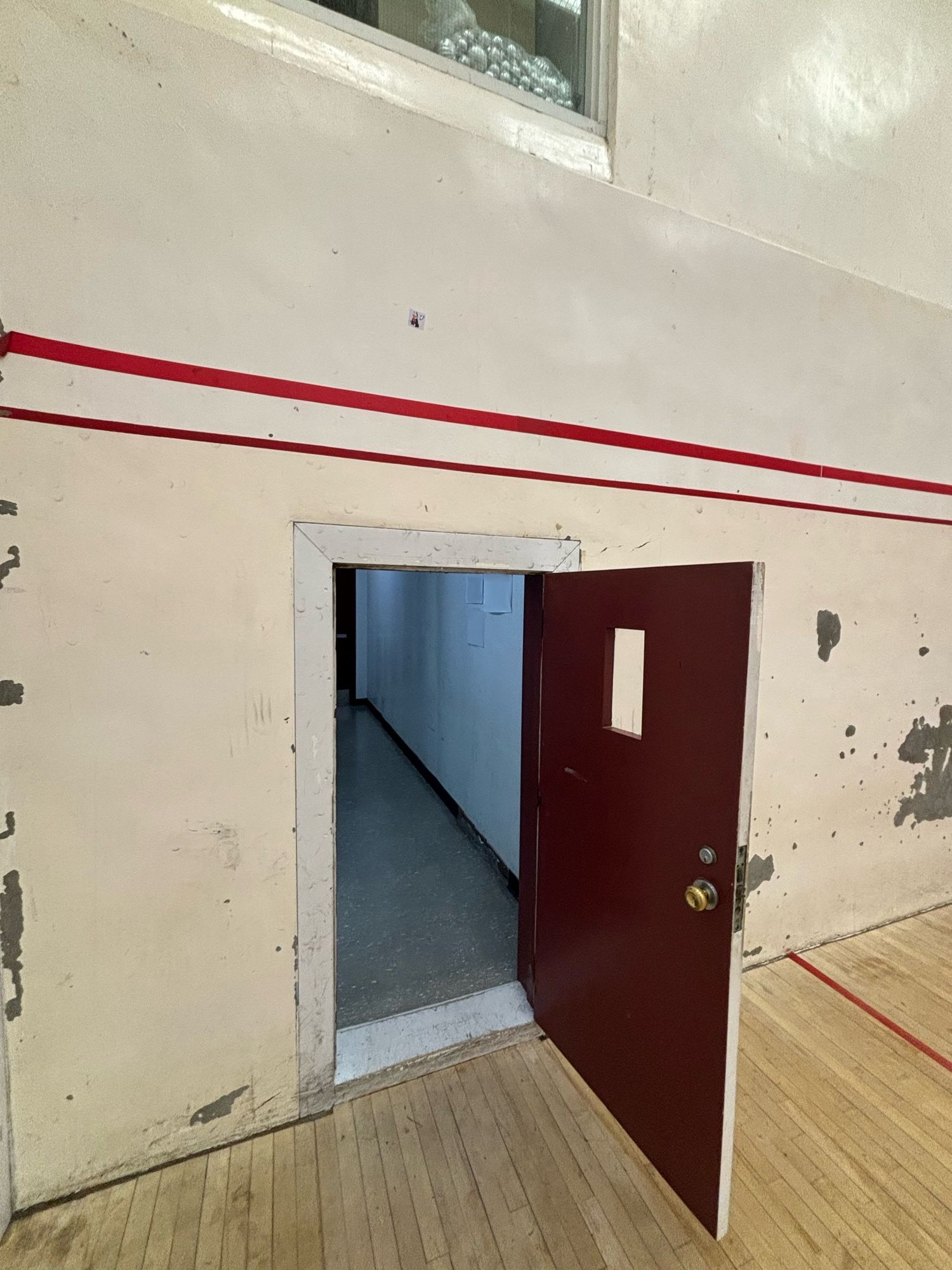 Old squash court with maroon door and viewing window