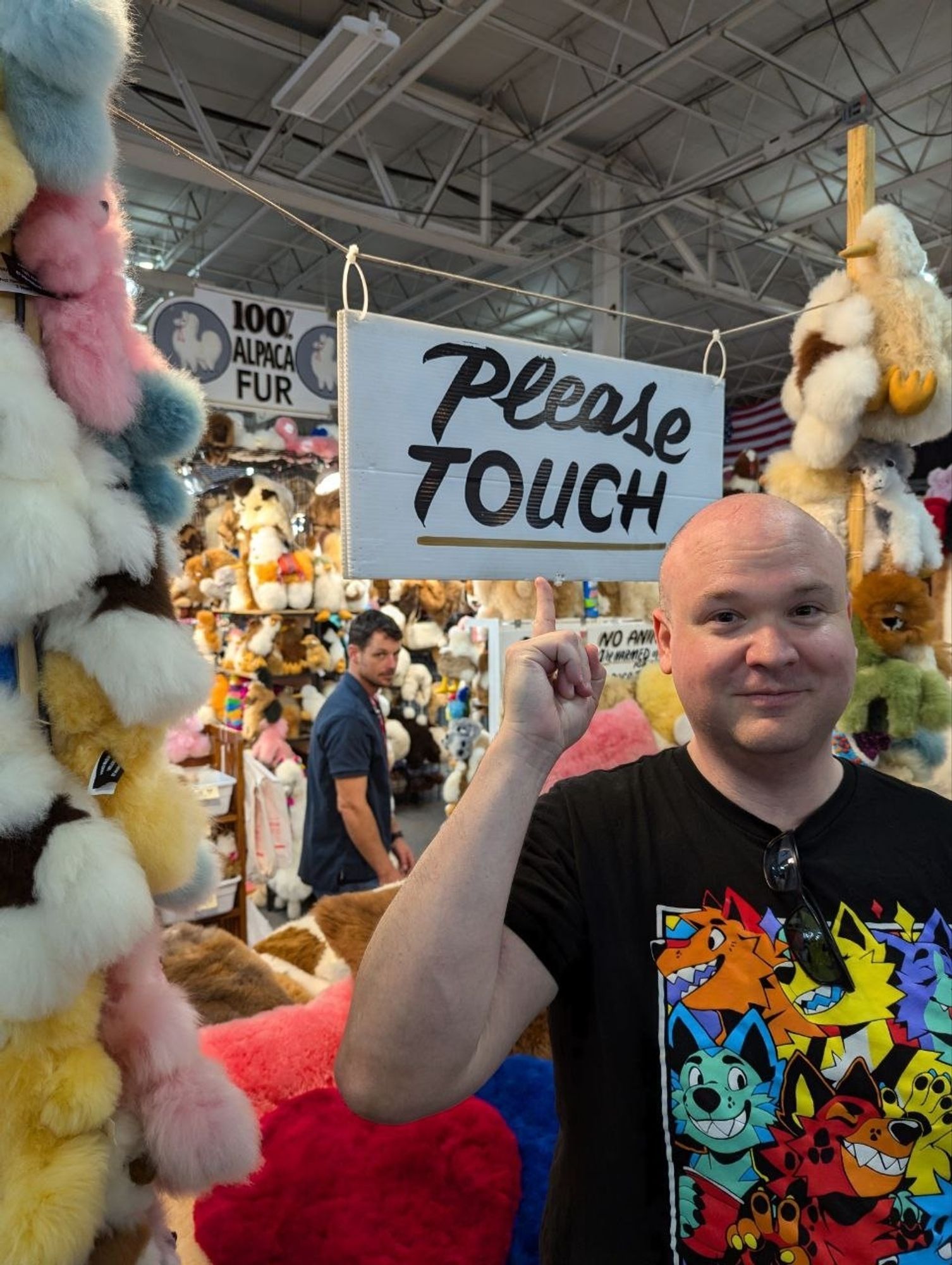 Dude standing in front of an alpaca booth at a state fair. A sign above him says "please touch"