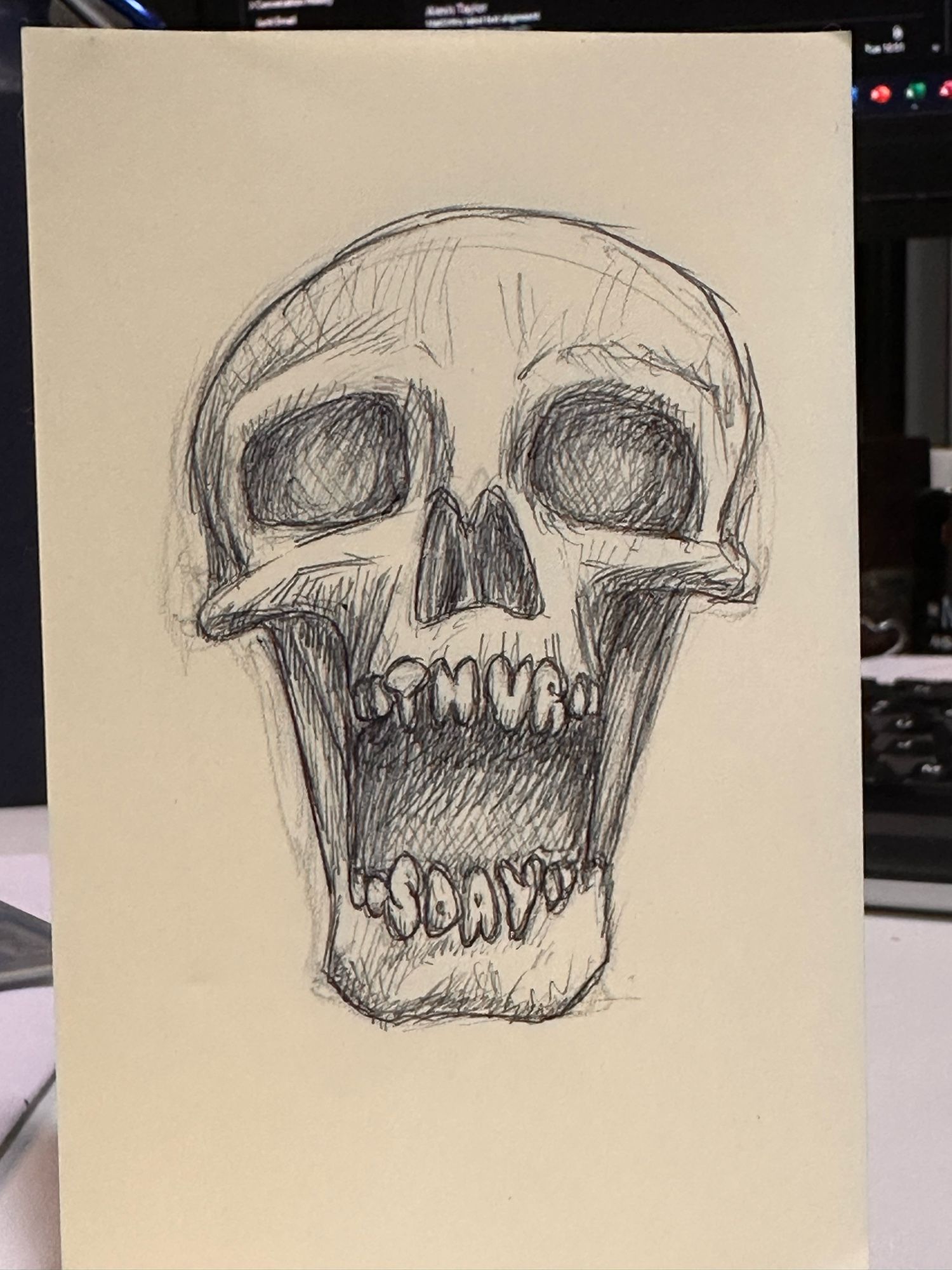 A scratchy drawing in black biro on a yellow post-it note, depicting a human skull with its mouth open in a silent scream, its teeth in the shape of letters spelling out ‘THUR’ in the top jaw and ‘SDAY’ on the bottom.