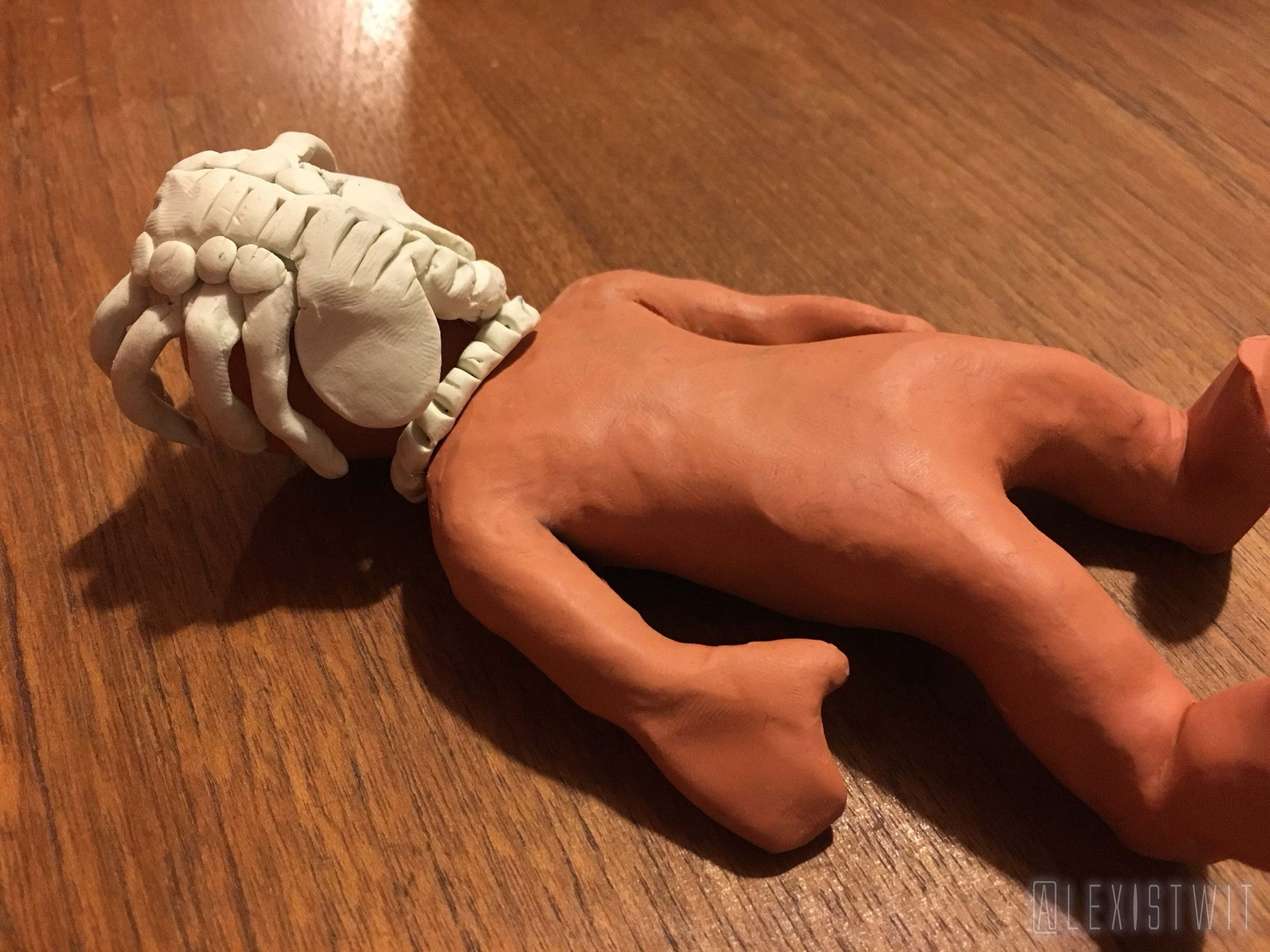 Morph lying unconscious on his back on the tabletop, the facehugger wrapped around his head, its tail tightly coiled around his neck