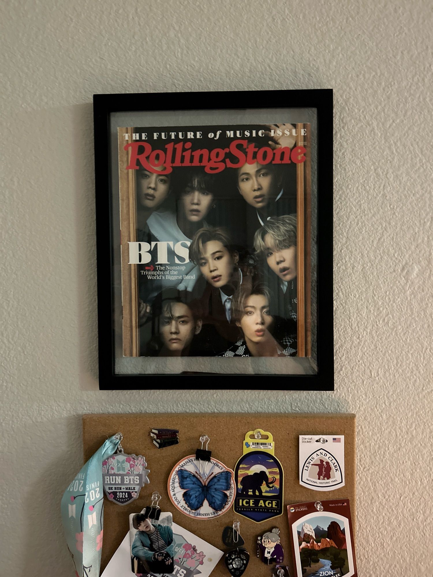 Framed copy of the June 2021 Rolling Stone BTS Edition. It shows the members crowded into a doorframe. I like to think it is the magic shop, but I don’t really know. Under the magazine is the top of a cork board with memorabilia from BTS fan events, including the annual 5K run/walk, a guitar pick and tag from Yunki’s D-Day concert in Belmont, and stickers from state and national parks in Arizona, Utah, and Nebraska.