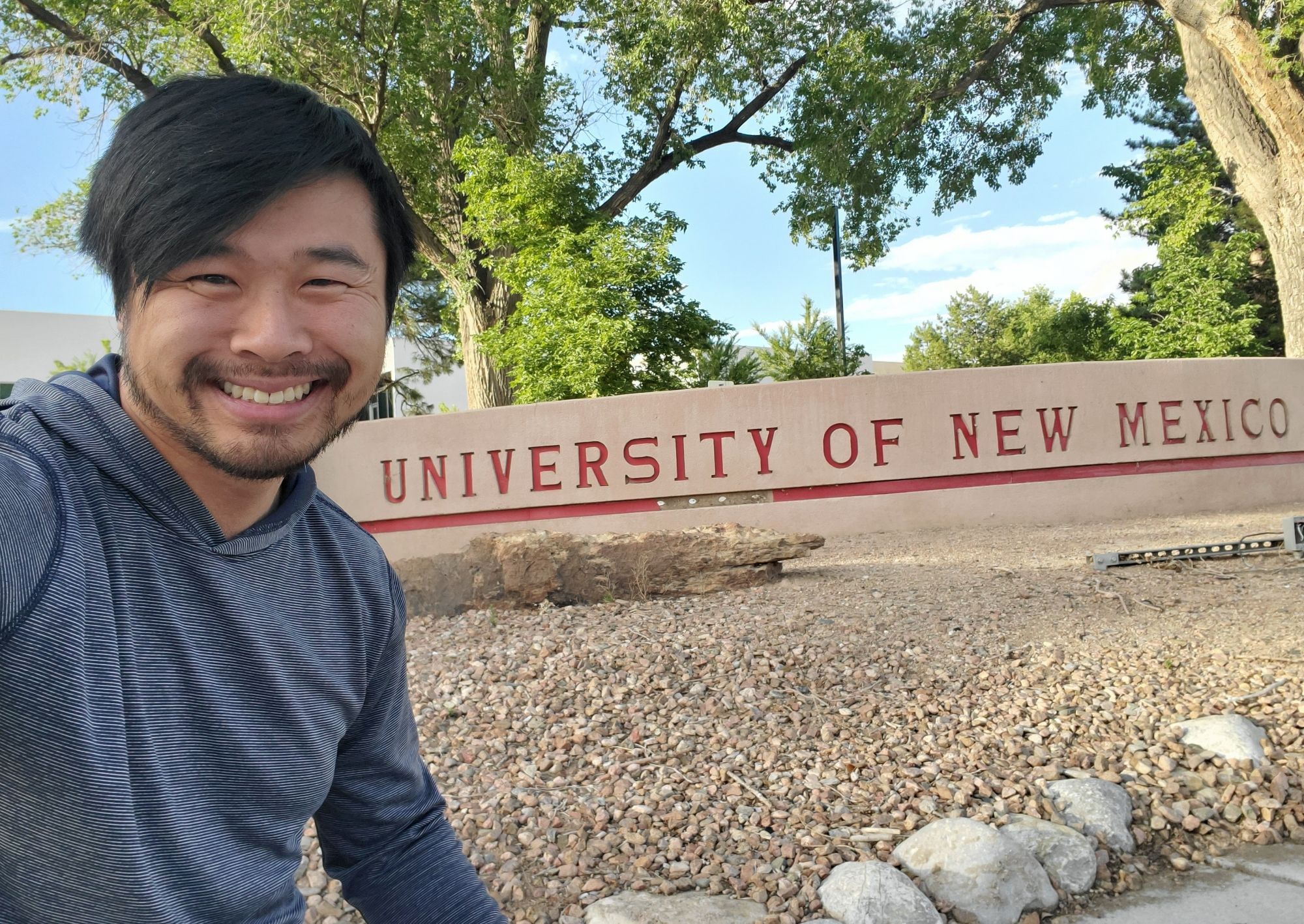 A selfie of me with a sign that says "University of New Mexico"