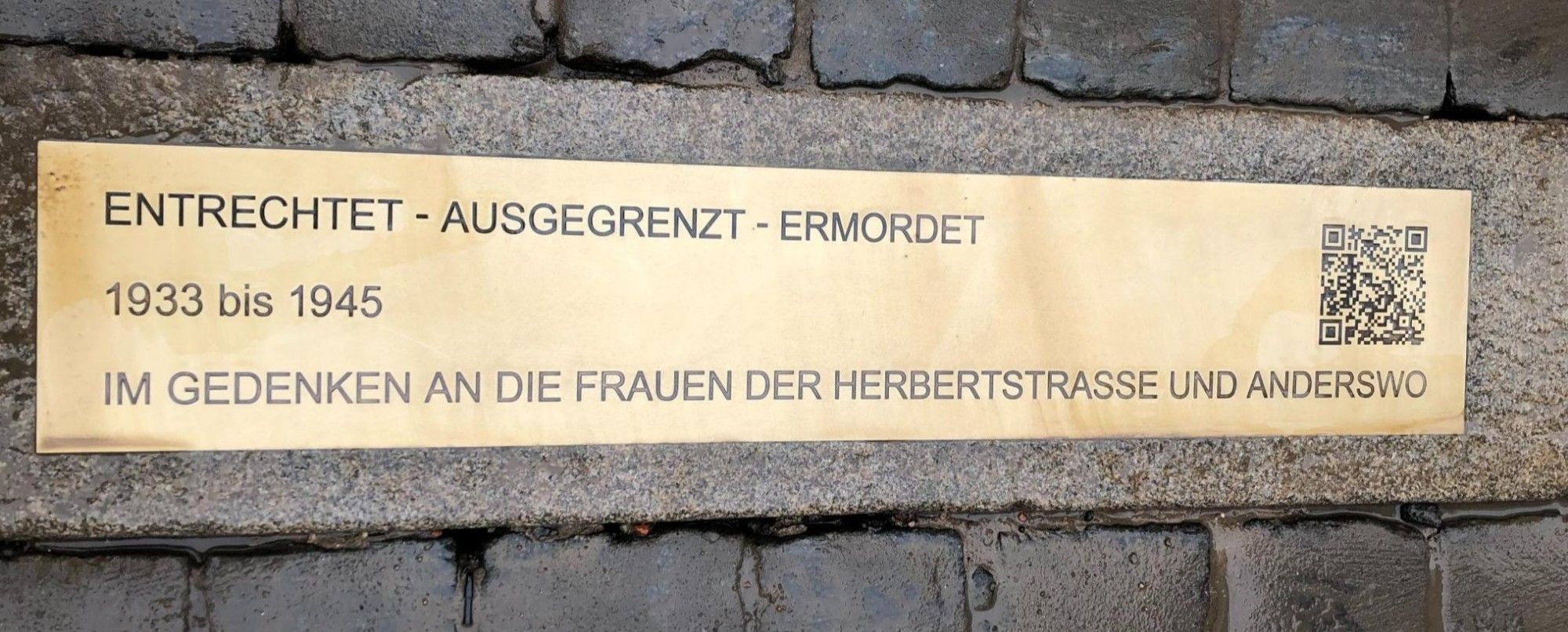 Auf einer Messingplatte steht:
ENTRECHTET - AUSGEGRENZT - ERMORDET
1933 bis 1945
IM GEDENKEN AN DIE FRAUEN AUS DER HERBERTSTRASSE UND ANDERSWO
PLUS EIN QR-CODE