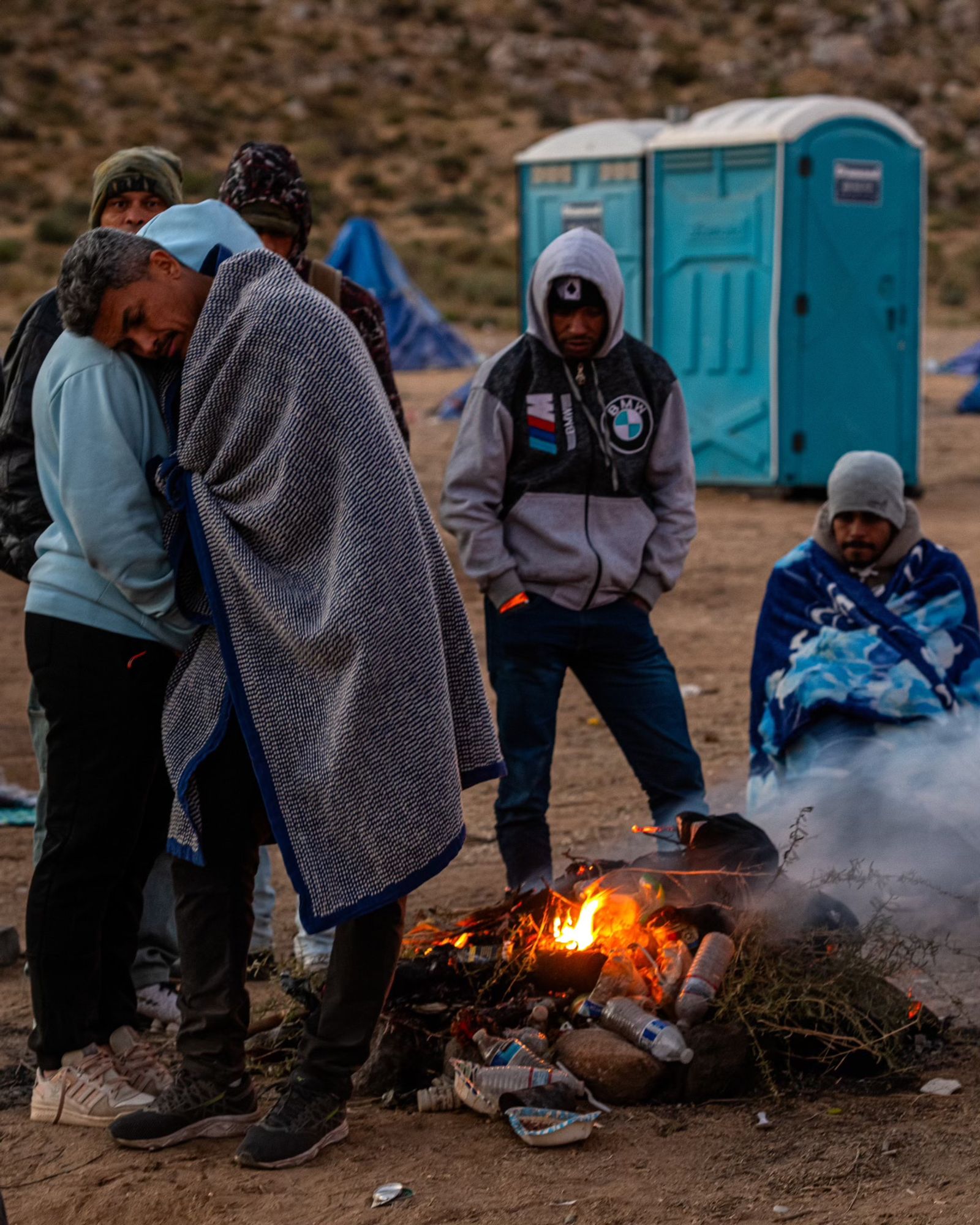 A couple stand together next to a fire in a desert landscape.

Caption: A Colombian couple huddles for warmth before dawn. Overnight temperatures at the Moon Camp fall below freezing and many migrants burn brush and rubbish to stave off the cold. (Ash Ponders for NPR)