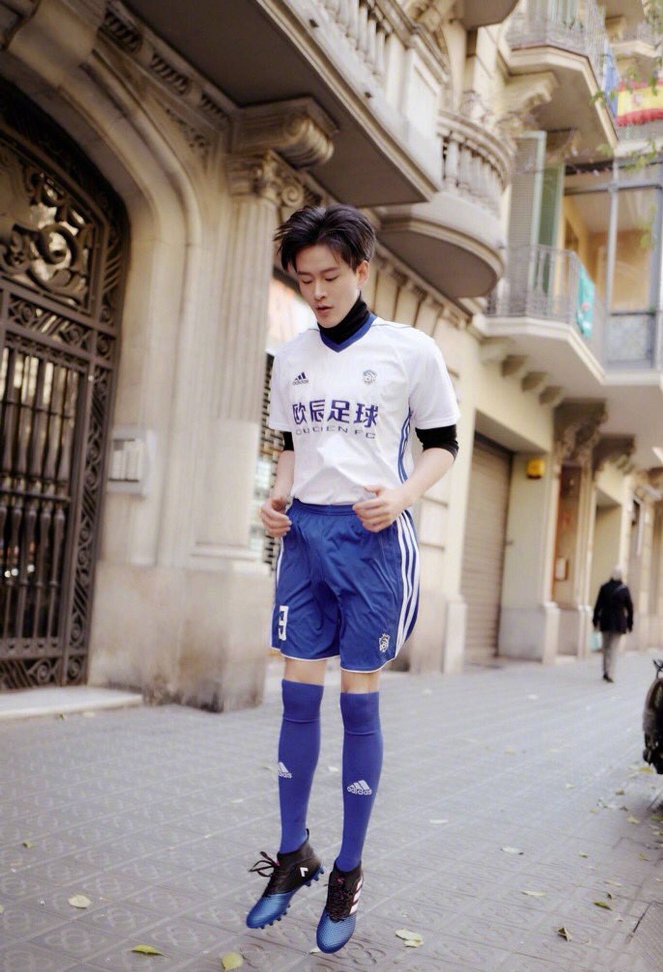 Huang Youming wearing a blue and white football/soccer uniform and jumping from standing. His shorts leave nothing to the imagination. Dude’s huge.