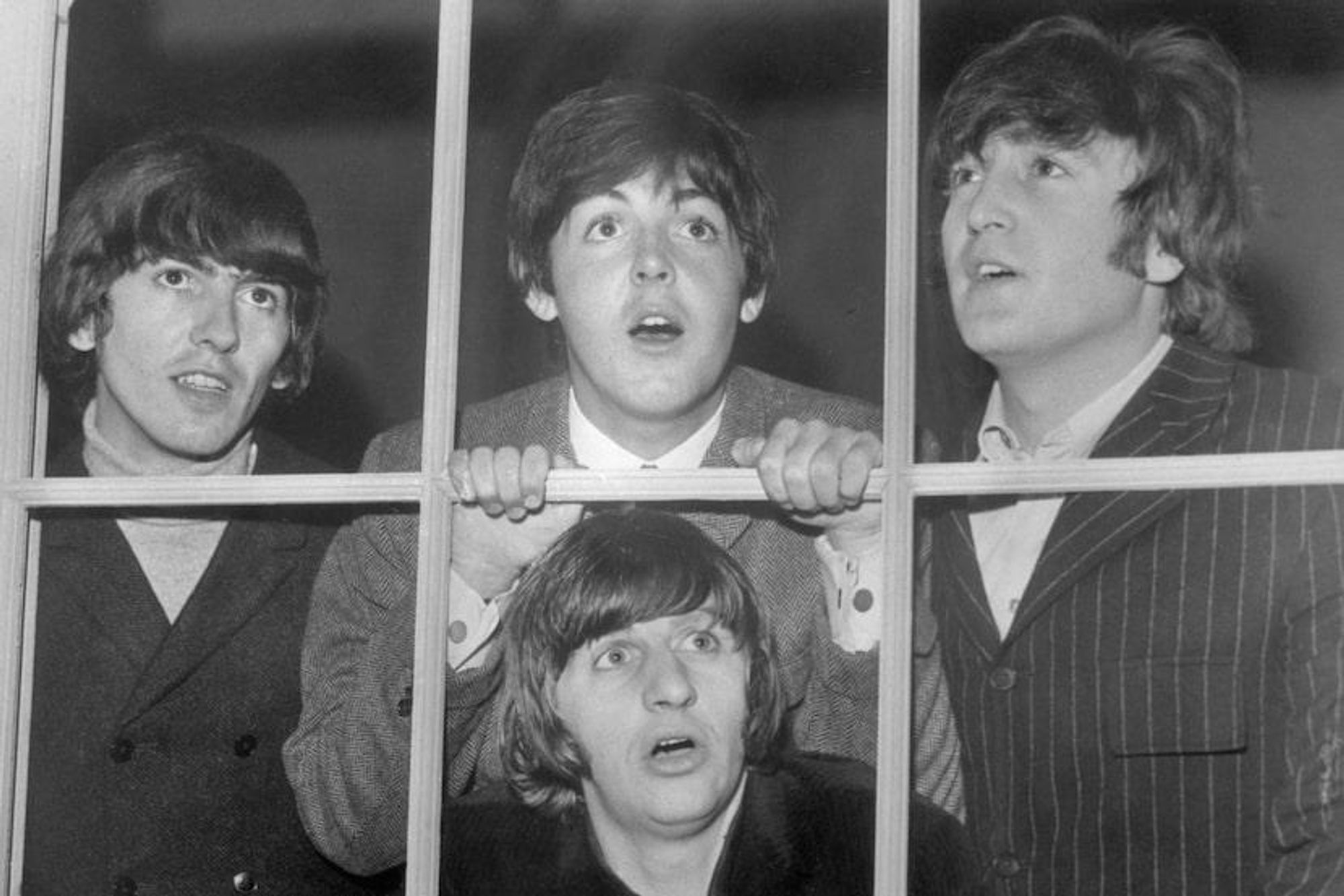 The Beatles behind a fake window (just a lattice wooden bars) are making funny faces. Ringo is at the center and behind him, George, Paul and John, all dressed in suit jackets