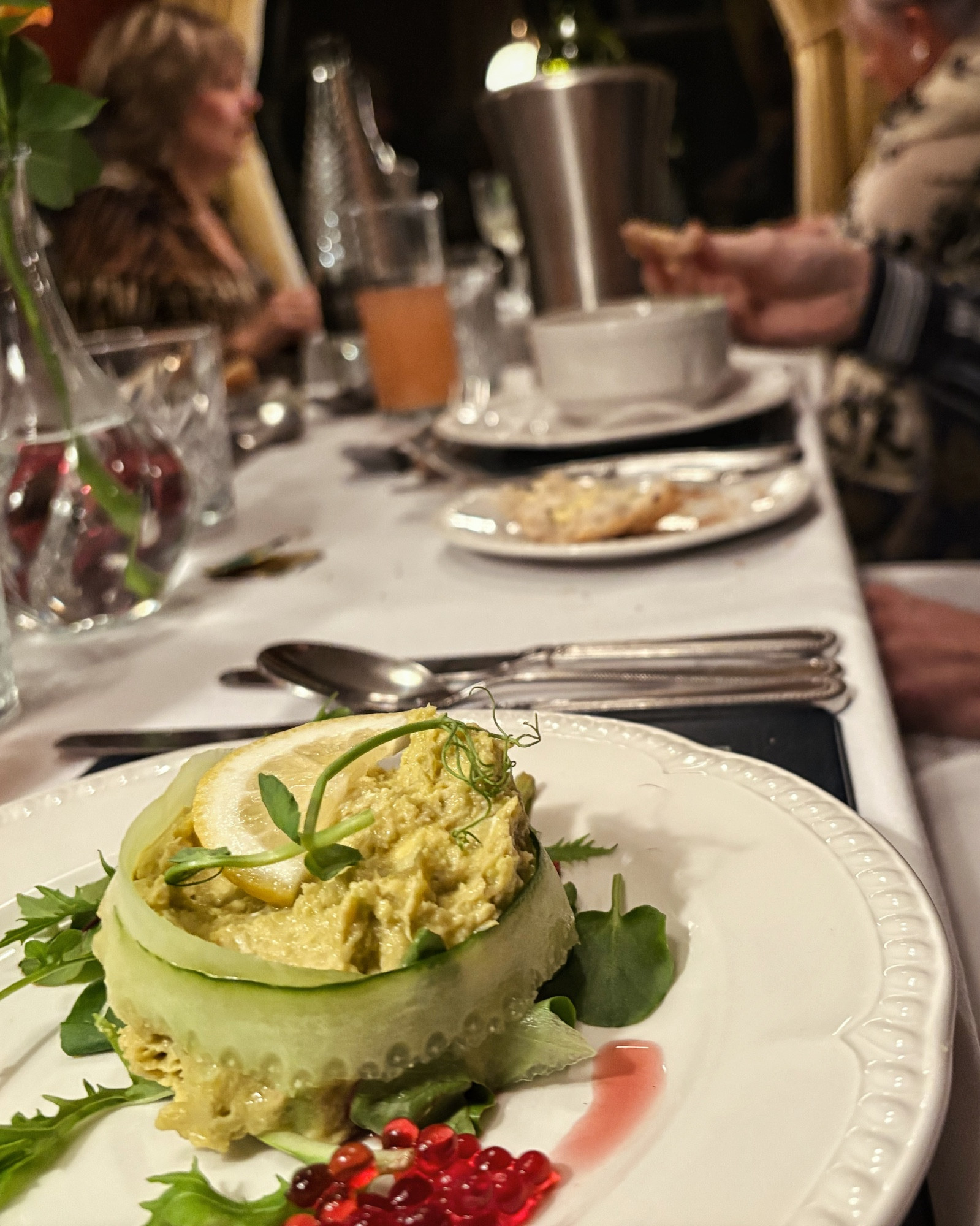 view along the table with a starter of crab and avocado in the foreground. my husband’s hand and soup, and fellow diners are blurry beyond.