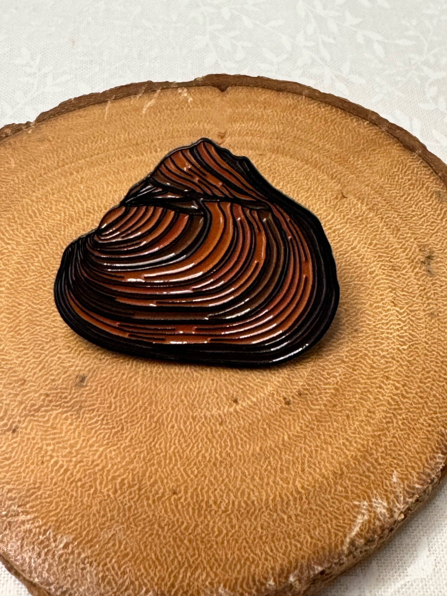 Close-up of a pink heelsplitter mussel enamel pin displayed on a circular wood slice. Perfect for nature lovers, aquatic biology enthusiasts, and collectors of unique, nature-themed accessories.