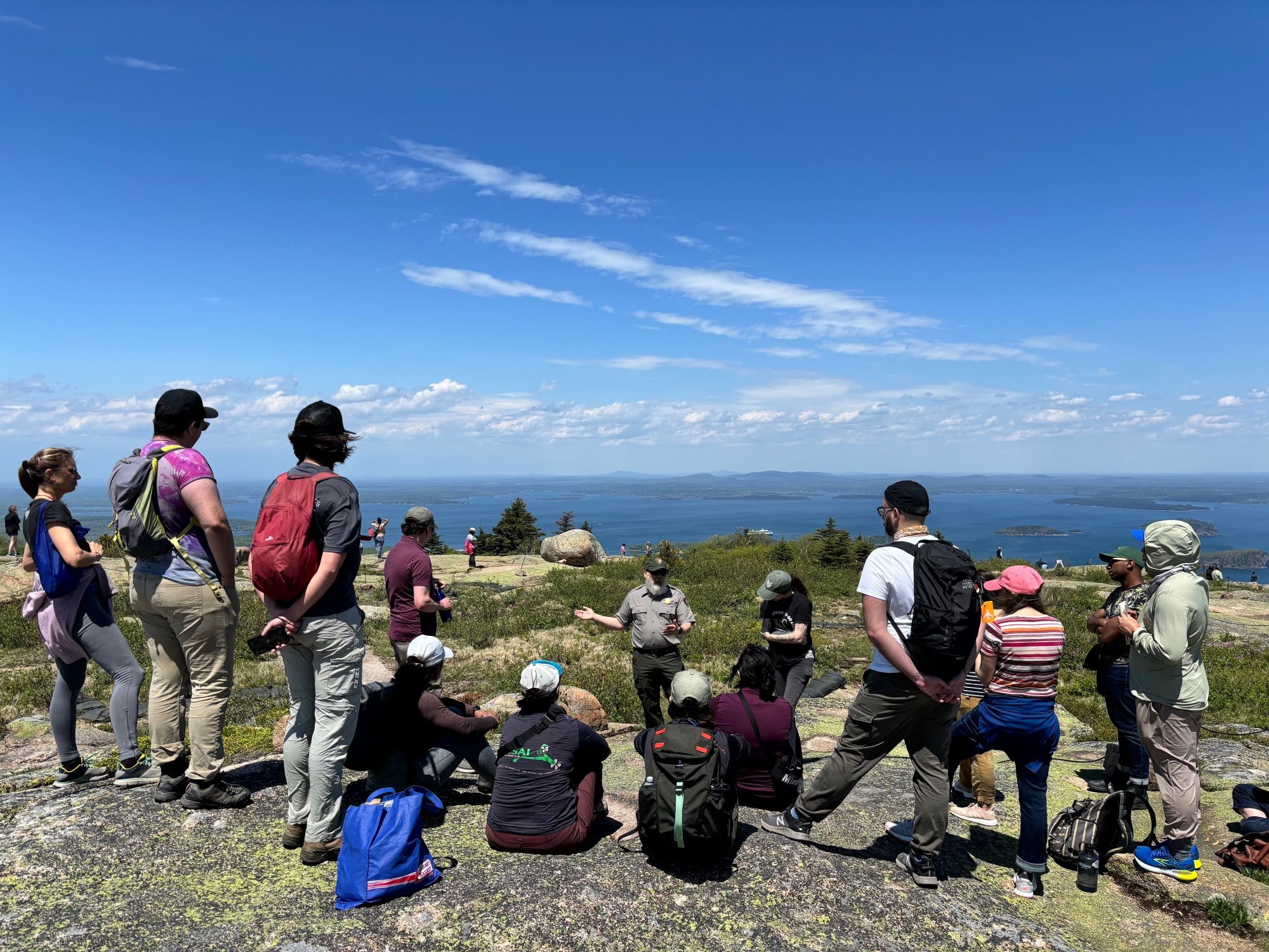 Fellows attending a ranger talk atop a peak overlooking coastal Maine