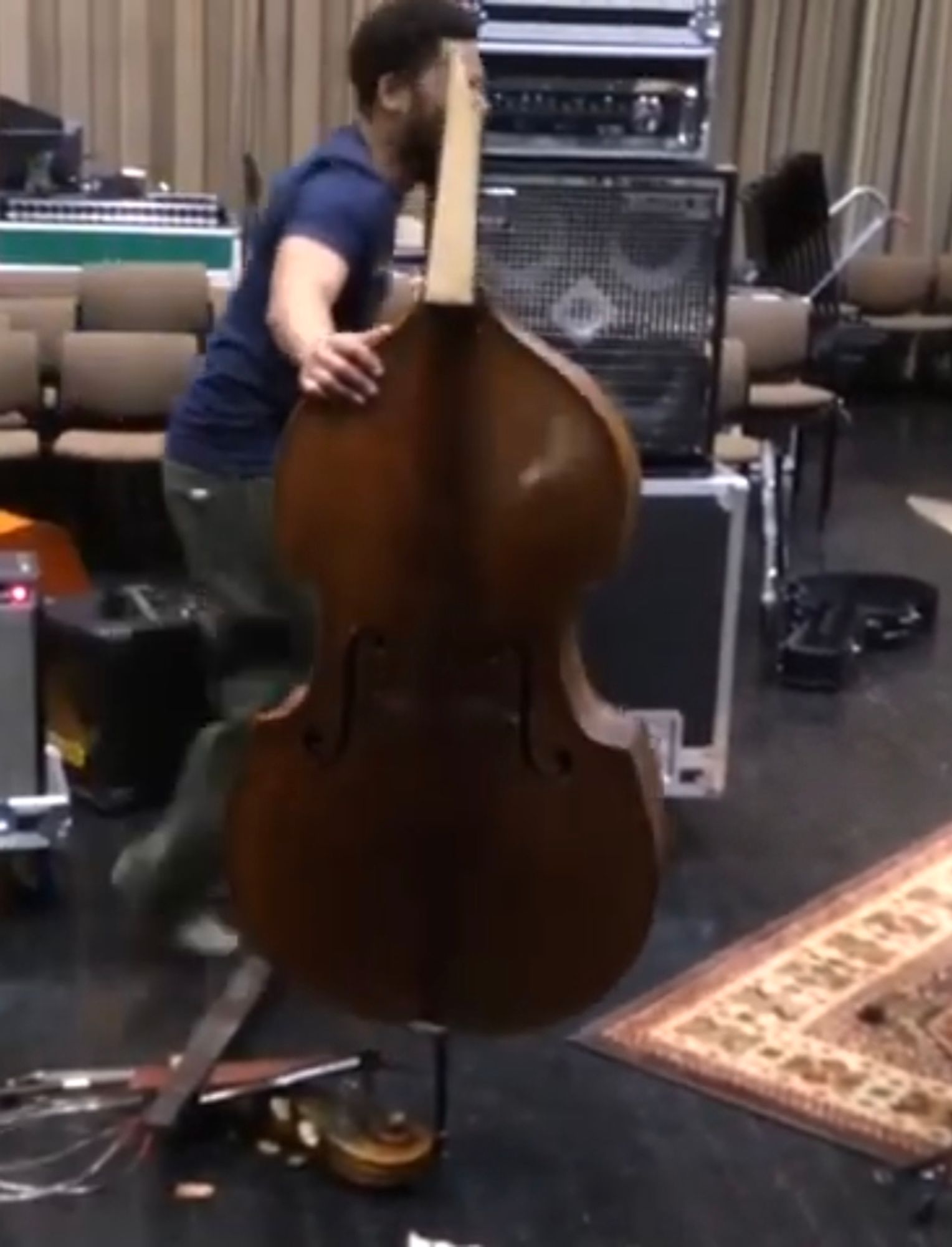 A man standing next to an upright bass with the neck snapped off and the bridge, neck, strings, and tailpiece lying on the ground