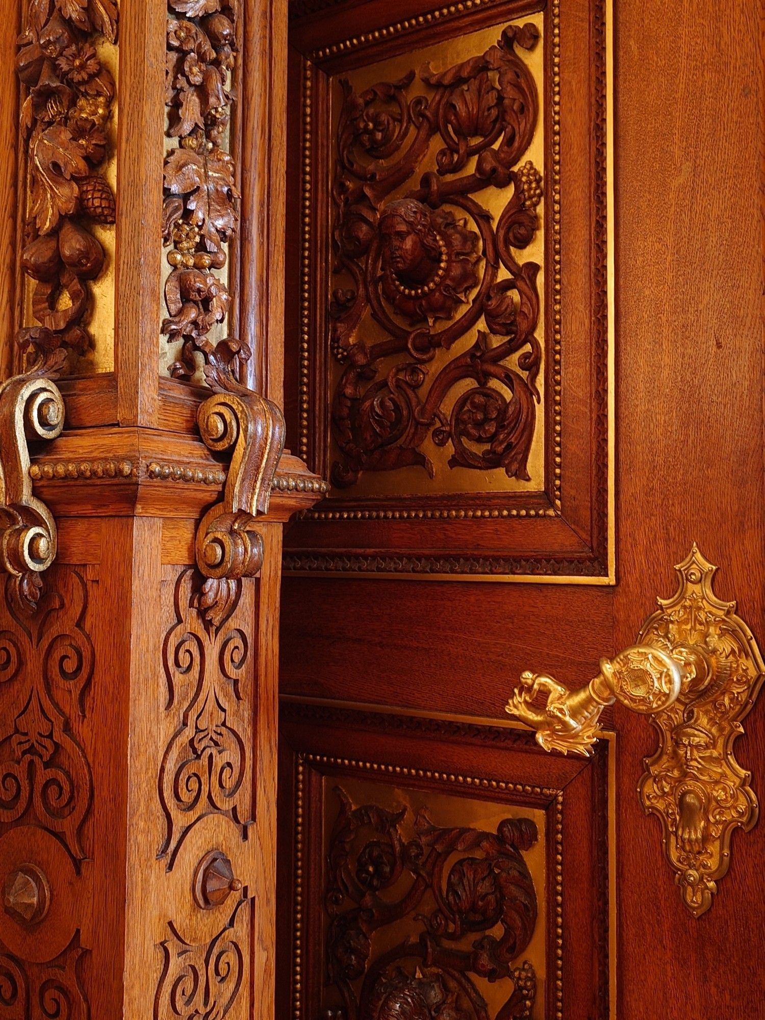 Ornate carvings in walnut wood and a gilded door handle that features a person fighting a beast