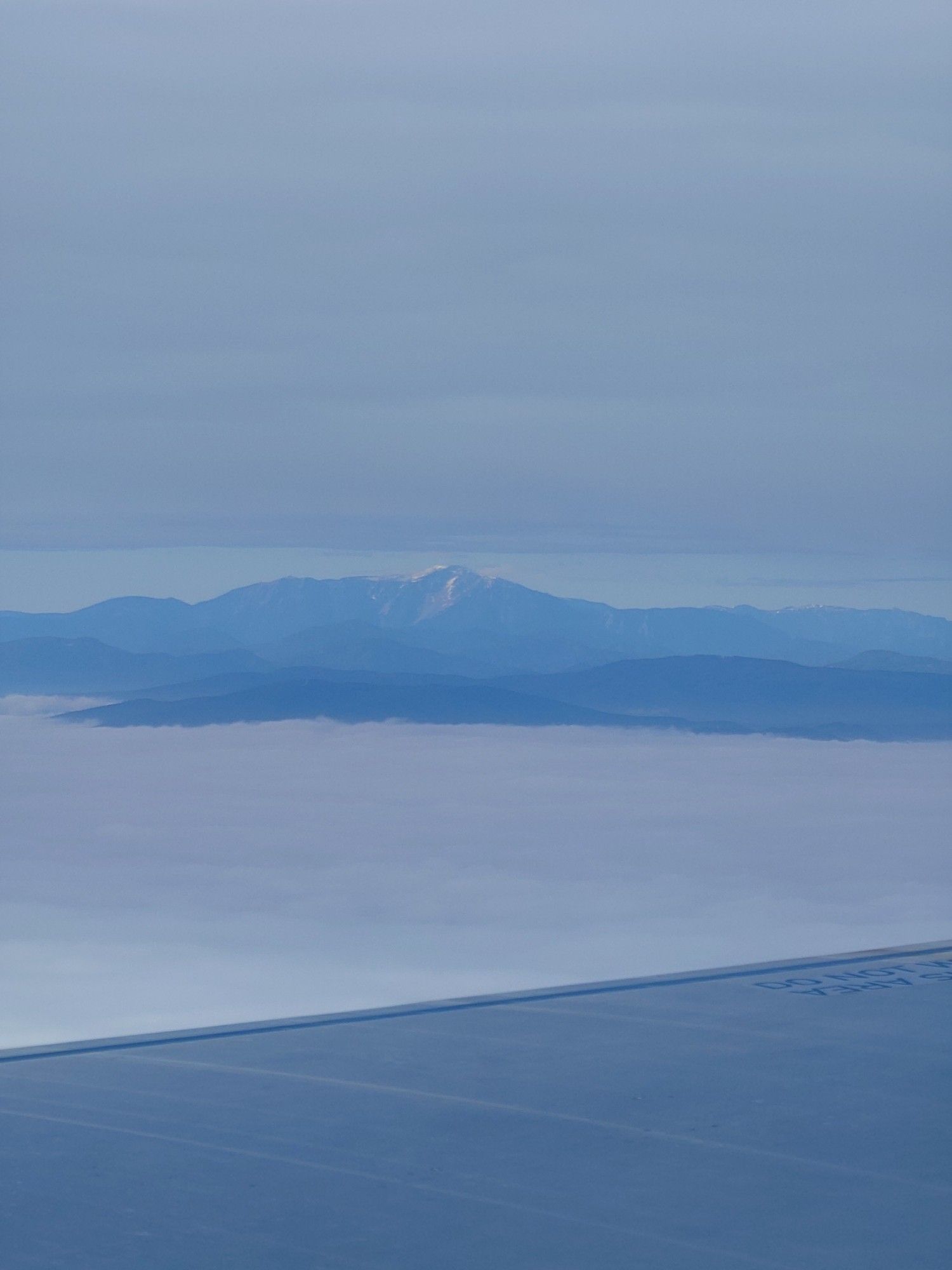 Mountains above the clouds. Plane wing in foreground