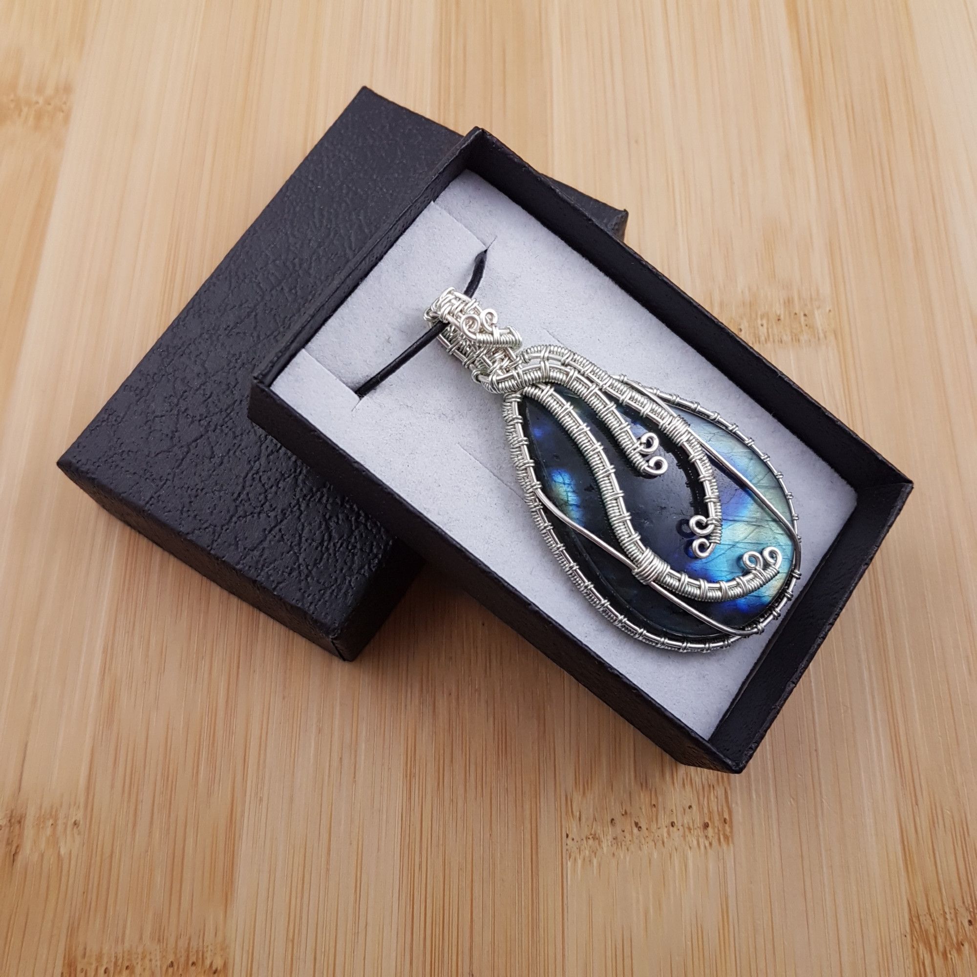 Large blue green drop pendant wrapped in wavy silver wire, sitting in black and white gift box.