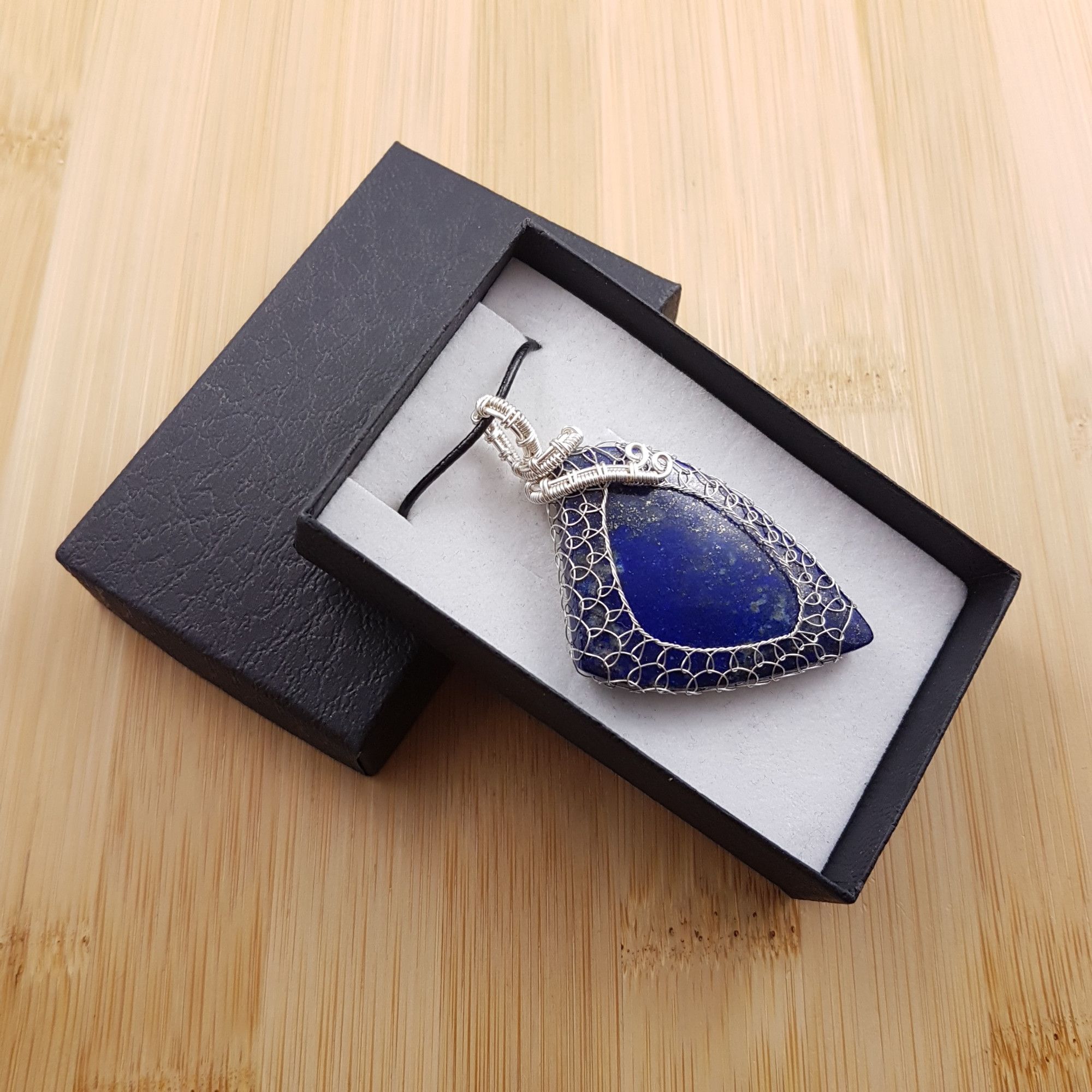 Angular blue pendant netted in silver wire, sitting in black and white gift box.