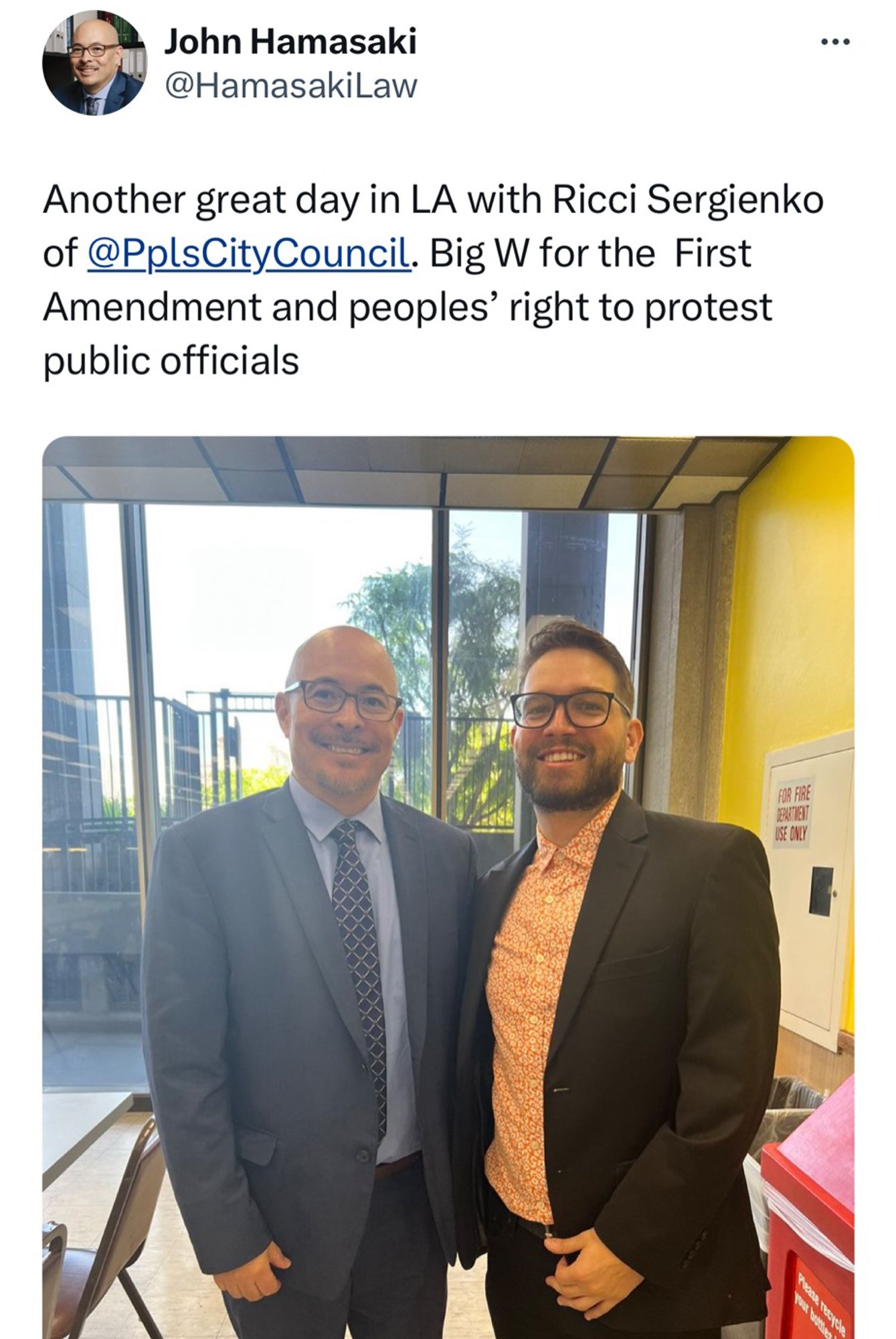 Tweet from John hamasaki says “Another great day in LA with Ricci Sergienko of @PplsCityCouncil. Big W for the  First Amendment and peoples’ right to protest public officials”

Picture of me and John. I have black suit and orange shirt. John in navy blue shirt, light blue shirt, & navy tie. Both have glasses. John is bald. 