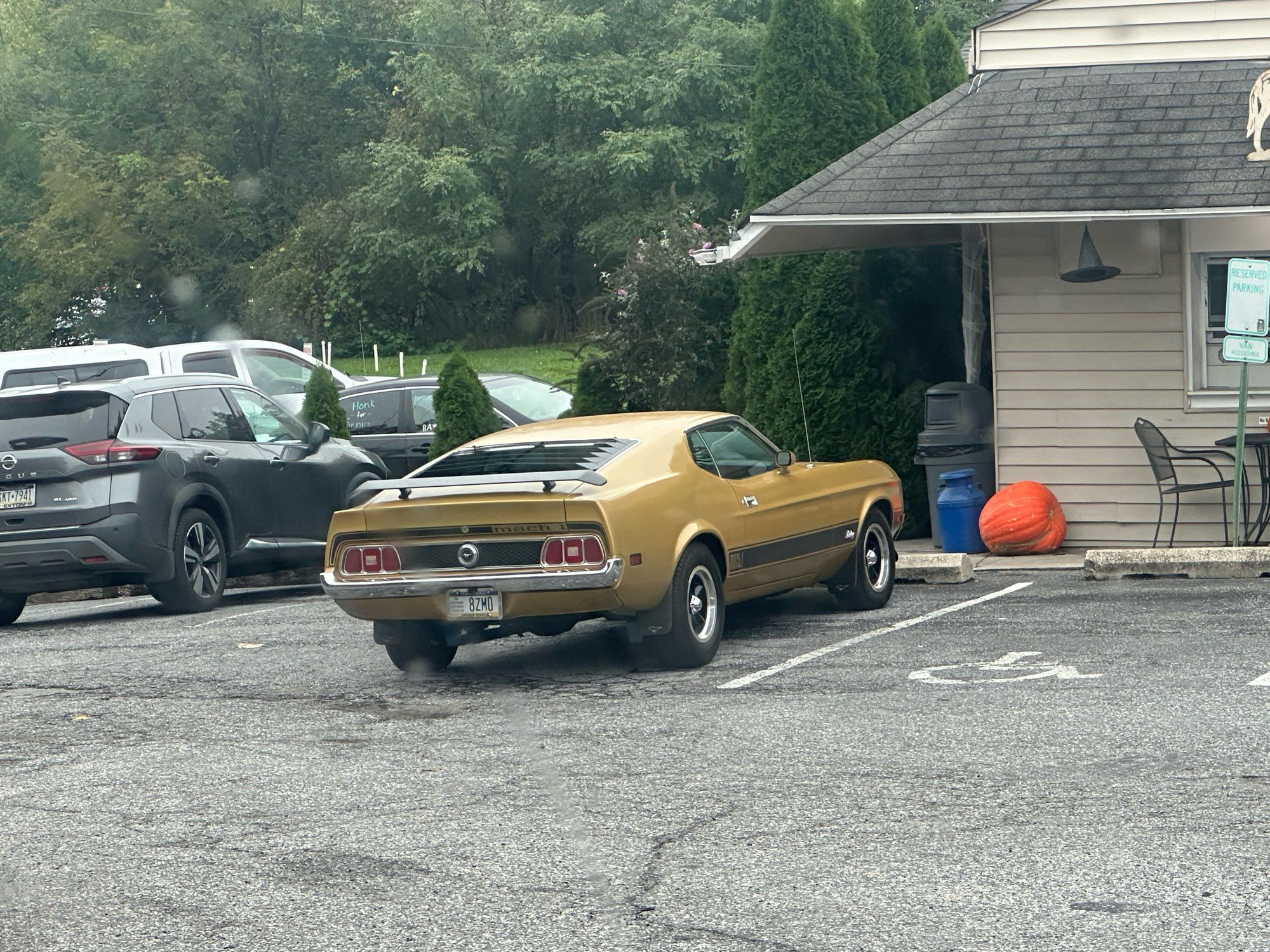 A bronze 71-73 Mustang Mach 1 parked in a parking lot in front of a small restaurant.