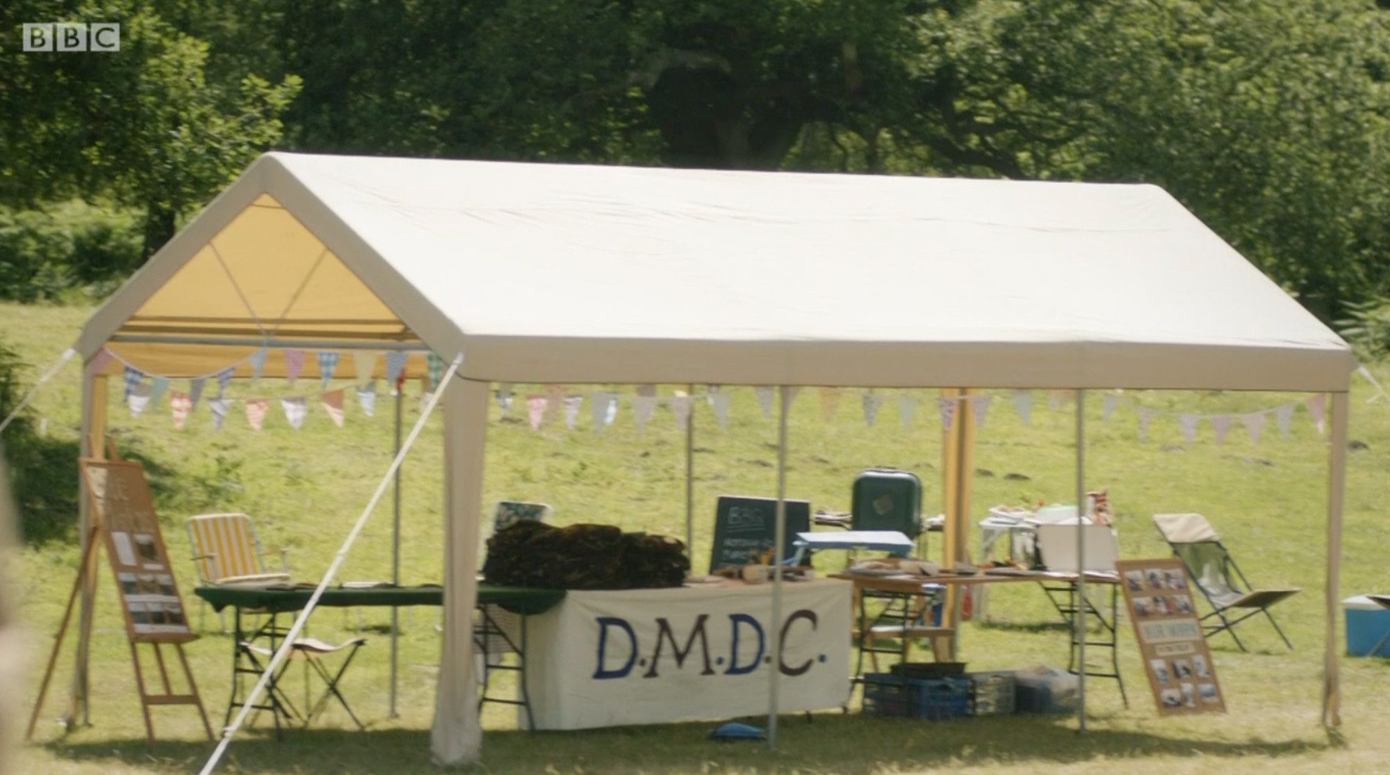 Terry's new gazebo from detectorists, showing a cream coloured gazebo with a few folding chairs and tables around, with a DMDC banner for their finds table