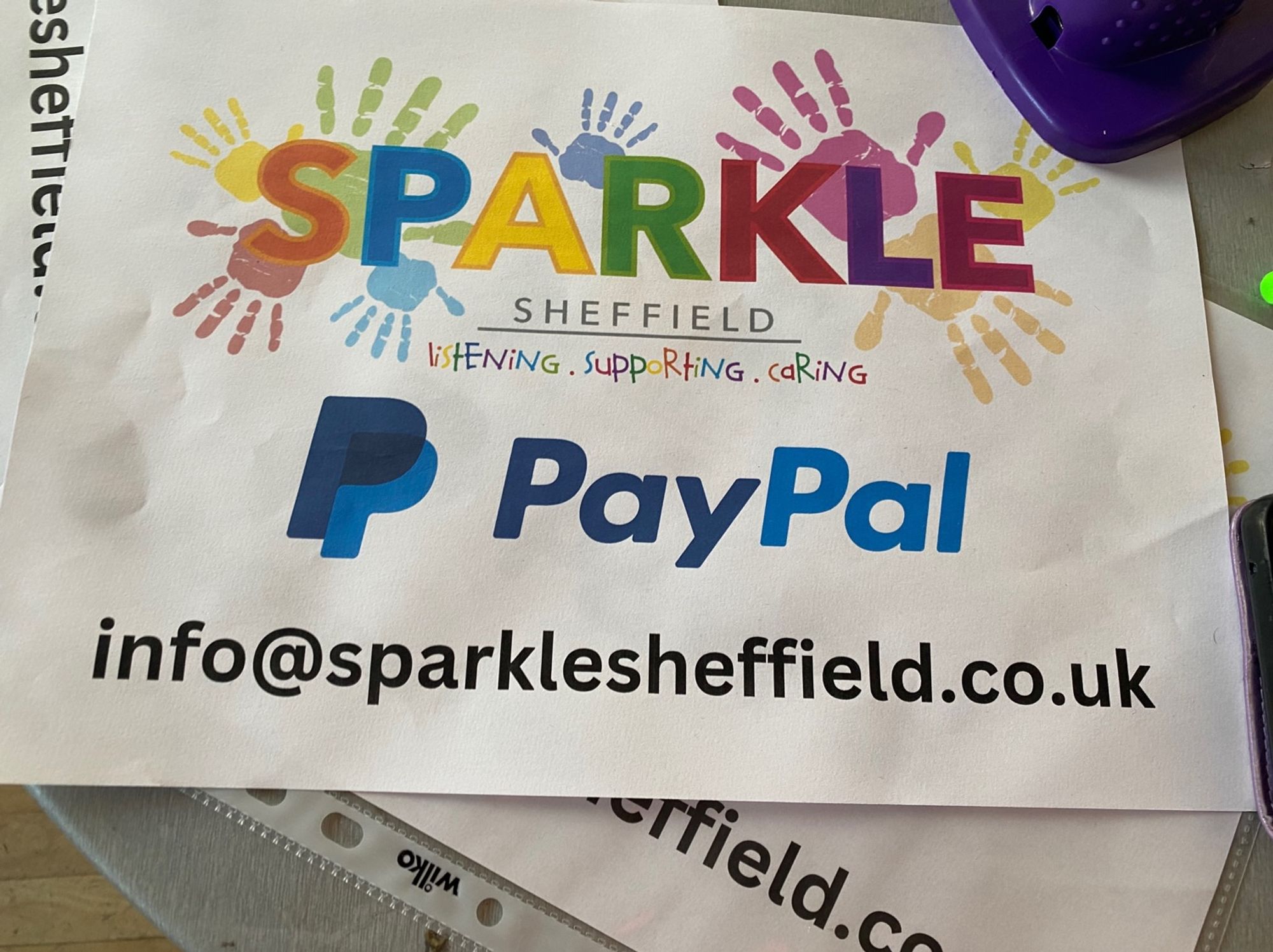 A photo of the sparkle Sheffield banner which is white. It has the sparkle logo, orange S blue pee, yellow A green R red K purple L pink E and multicoloured children’s hands to look like lots of paint. The PayPal information/ email on get banner  is info@sparklesheffield.co.uk