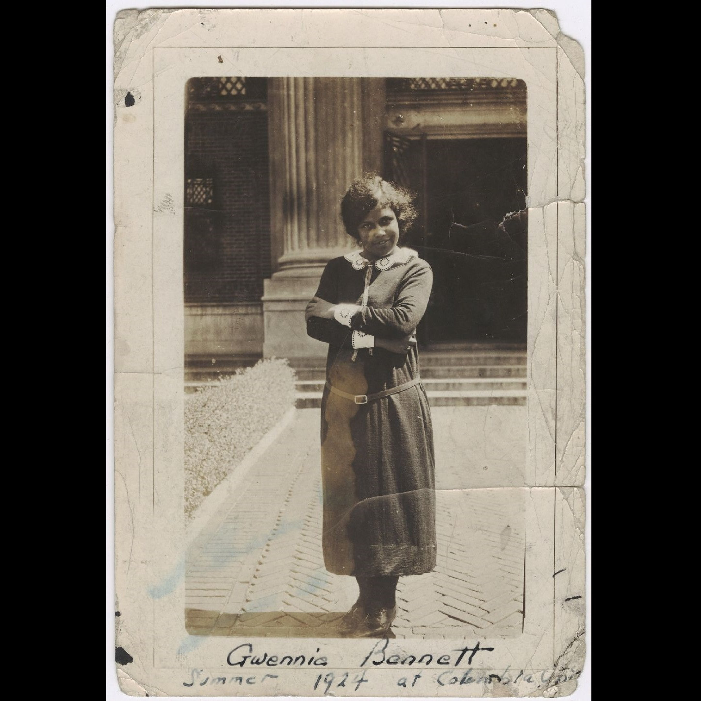 Photographie en noir et blanc.

Une jeune femme noire se trouve debout à quelques mètres de l'imposante colonne d'un bâtiment officiel. Elle porte une longue robe noire ceinturée à la taille et pourvue d'un col en dentelle blanche.

Au bas de la photo, on peut lire, écrit à la plume :

"Gwennie Bennett
Summer 1924 at Columbia Uni."