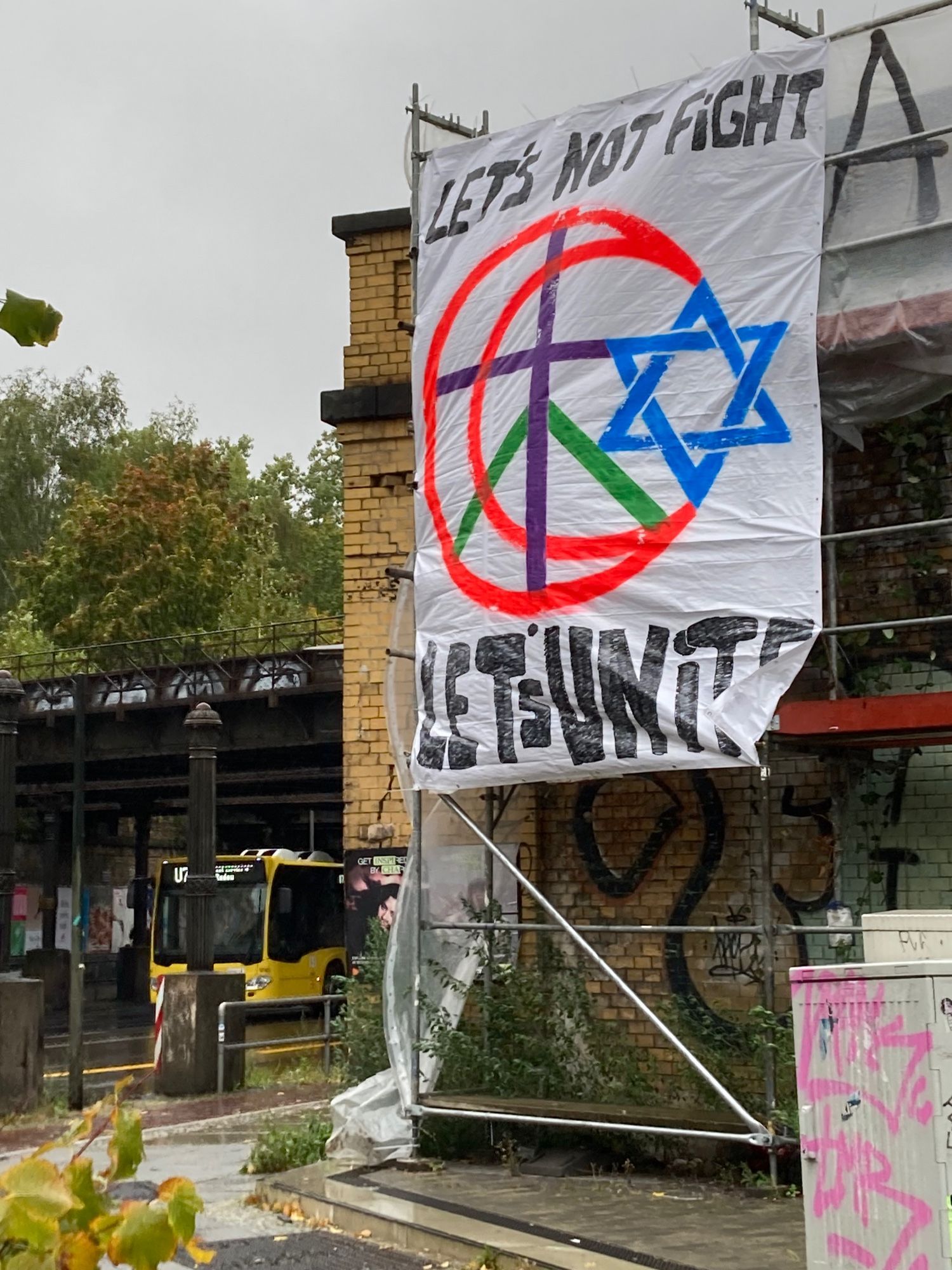 Foto eines Plakates mit einer palästinensischen und israelischen Flagge, die vor einen Peacesymbol verschmelzen. Die Inschrift auf dem Plakat lautet: Let’s not fight, let’s unite!