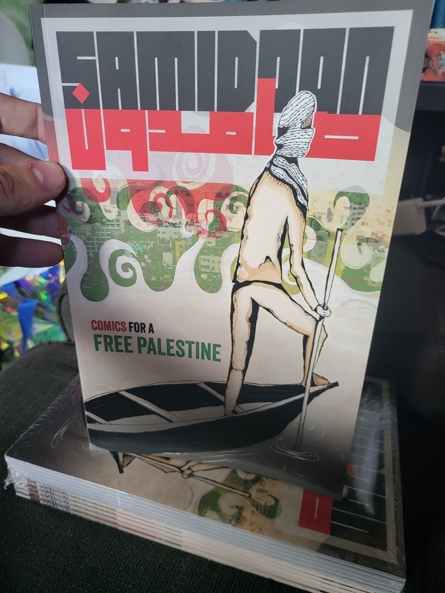 The cover to Samidoon as a real book held in my hand on a stack of 10 more copies. 