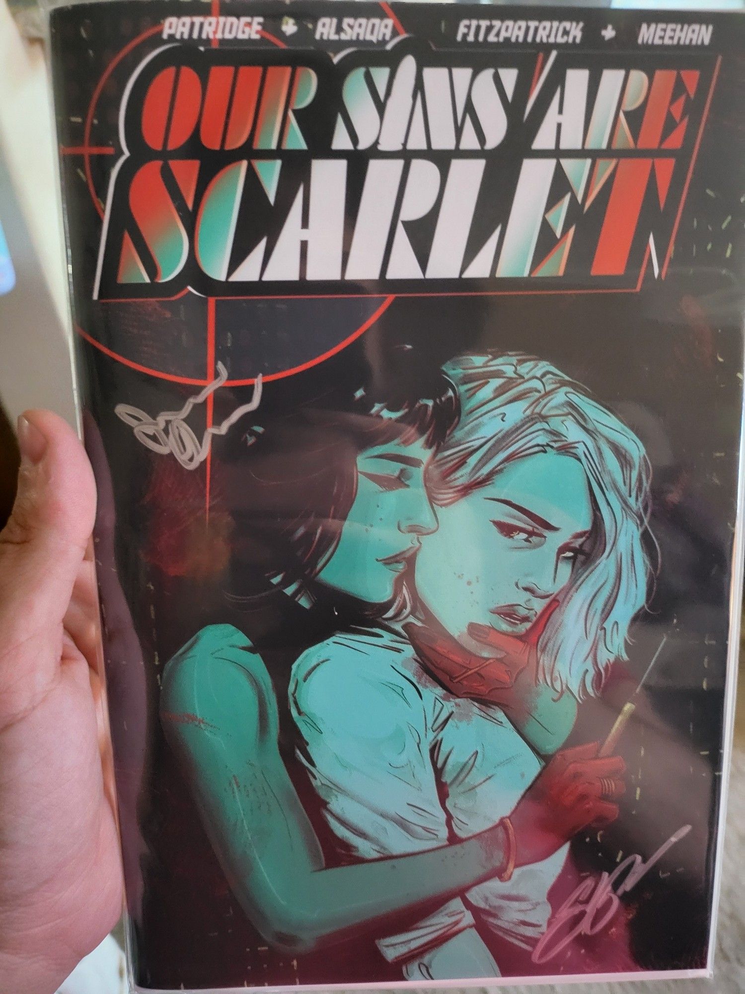 My hand holding the first issue of Our Sins Are Scarlet. The cover is largely blue-green and red. A woman holds another woman from behind seductively but also threateningly.