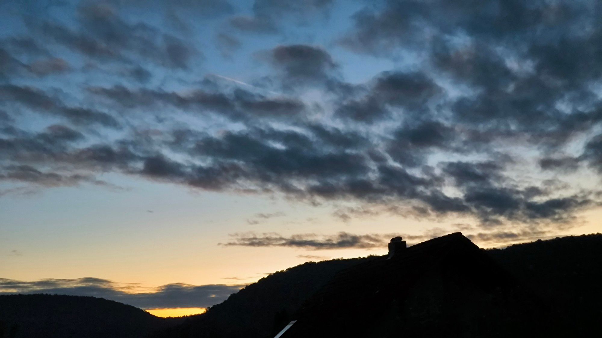 Man kann die Sonne irgendwo hinter dem Berg riechen. Der Himmel ist teils orange.