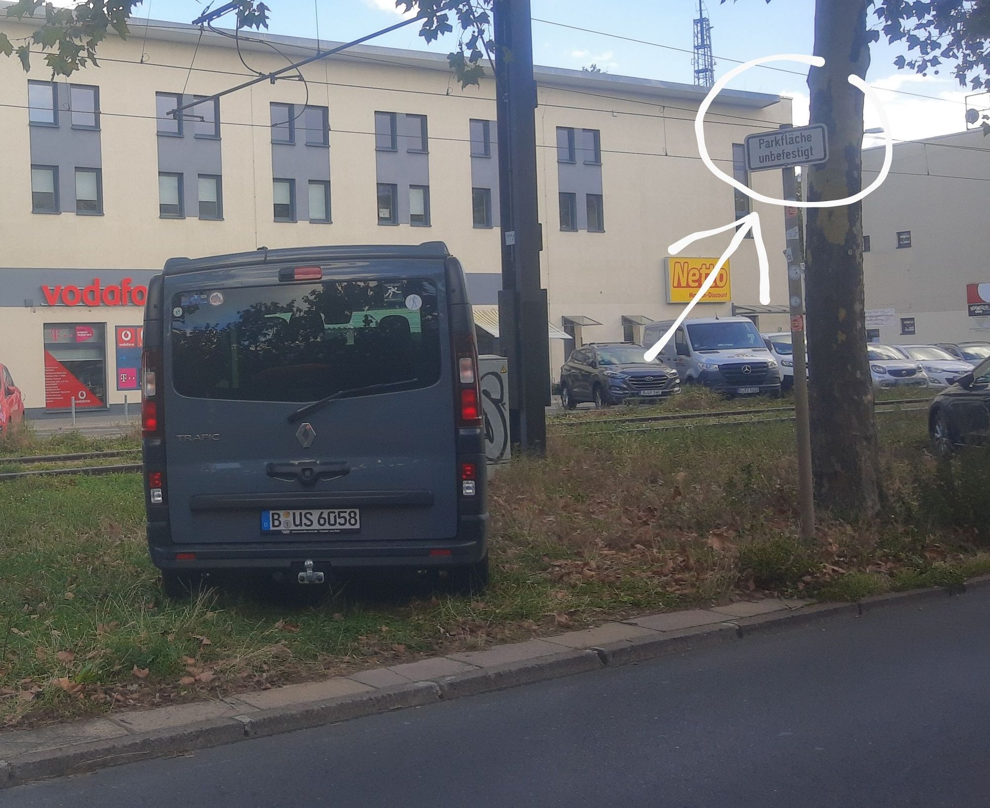 Auto parkt auf der Wiese, daneben Zusatzschild "Parkfläche unbefestigt"