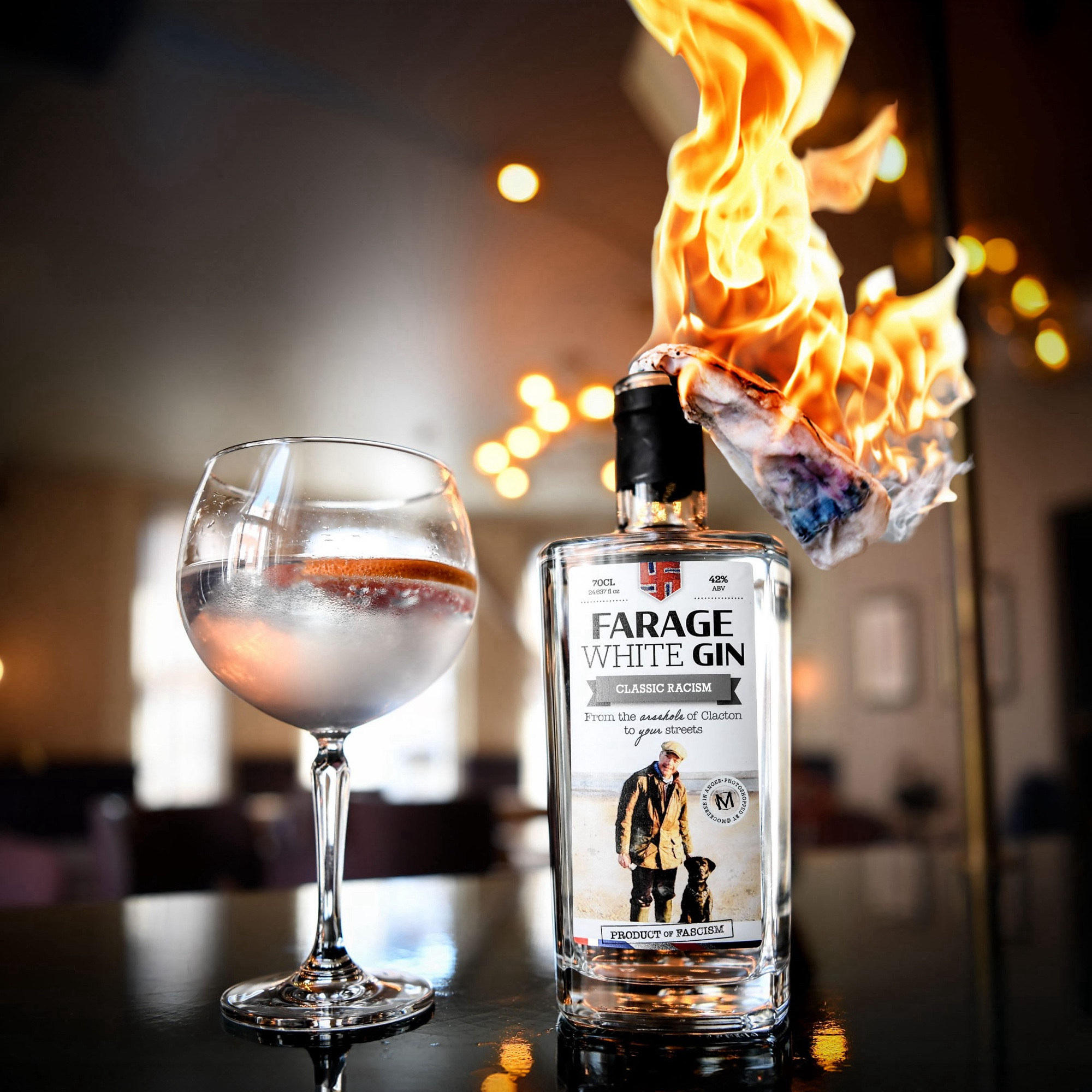 An edited Farage Gin advert. In close-up on a dark wooden table in a bar, a glass sits next to a bottle of Farage White Gin (because obviously) with a burning rag stuffed in its neck. On its label, the Union flag has got swastika crossbars, the slogan now reads “From the arsehole of Clacton to your streets”, and it describes itself as “classic racism” and “product of fascism”. A circular stamp says “photoshopped by @mockeree in anger”, because it was.