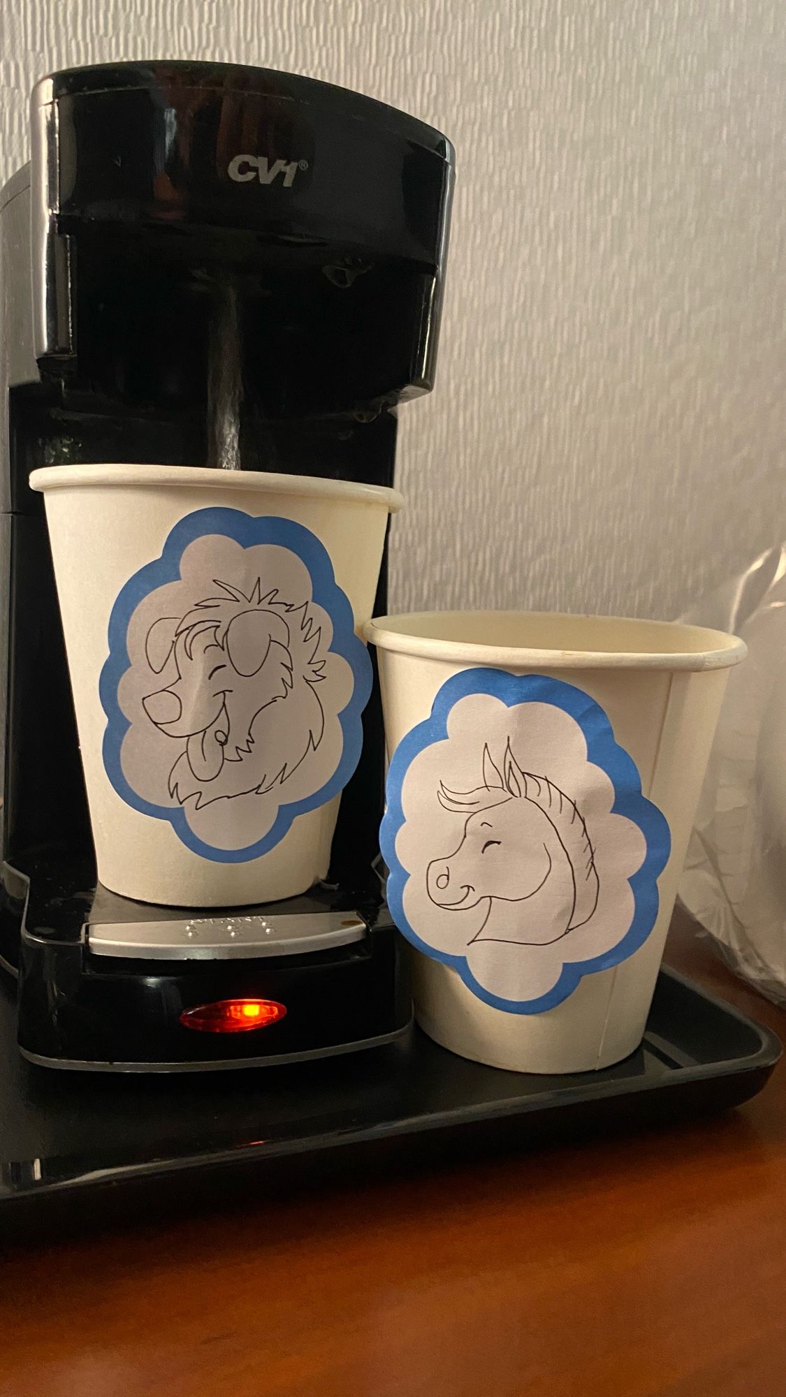 Two paper coffee cups with a post-it note drawing on each.  The left one (brewing coffee) has a cool dog drawn on it.  The right one has a gross pony who smells and is icky on it.