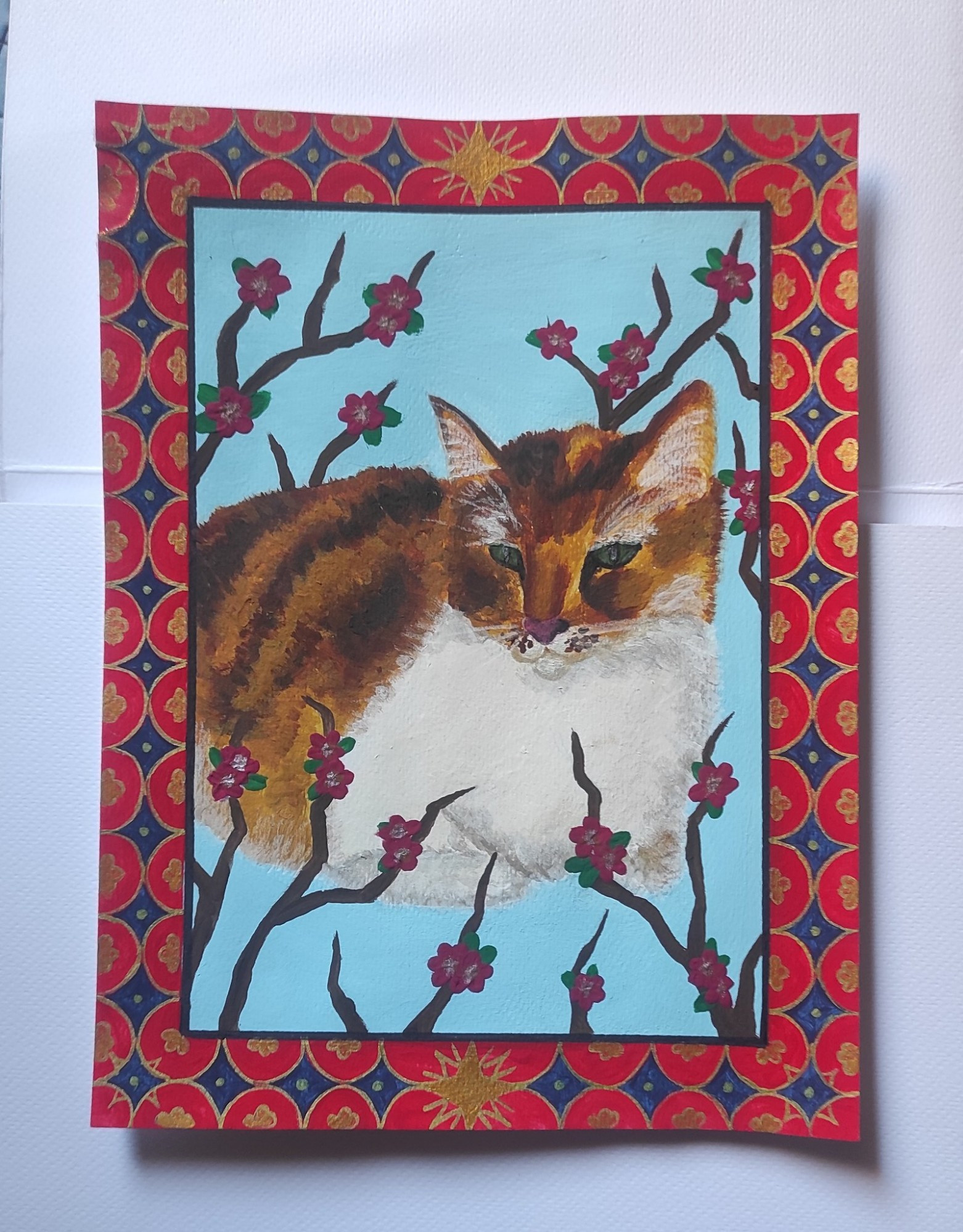 A small painting of an orange striped cat, surrounded by pink flowers. 