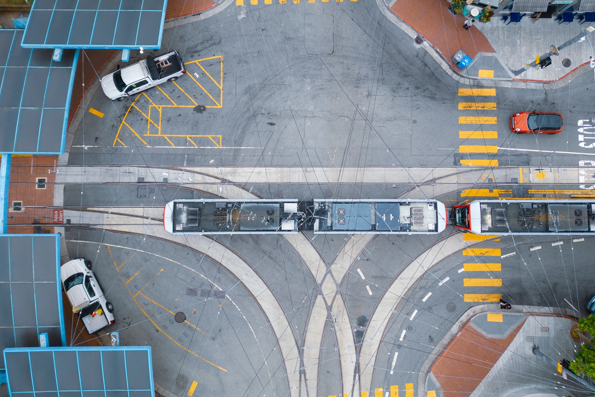 A track wye as seen from directly overhead on the street outside the station, with a train exiting. There is a pattern of tire marks in the intersection, and a spiderweb of wires going across.