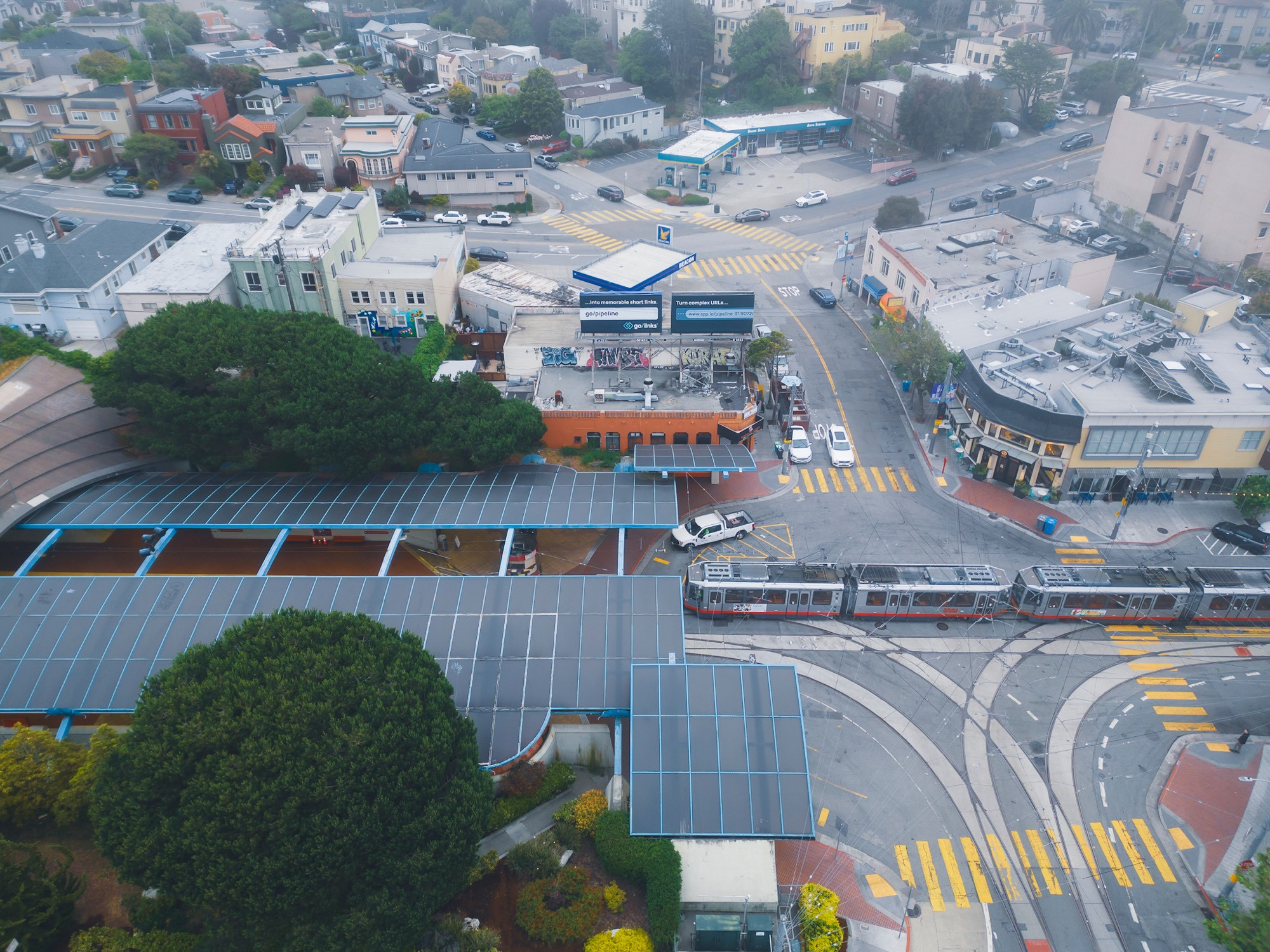 The station and intersection as seen from an elevated angle. Beyond them is a foggy view of a gas station, houses, and short commercial buildings.